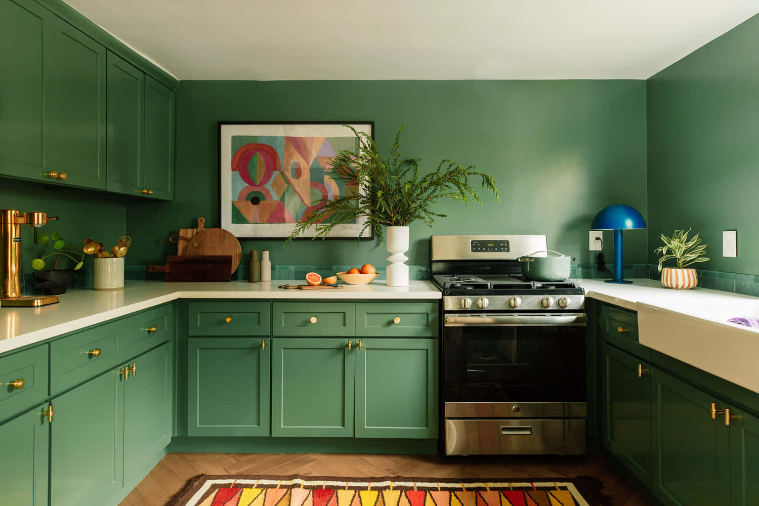 Kitchen Design 桌布 壁紙 — 一個充滿活力的綠色廚房，配有金色五金件、白色檯面和色彩繽紛的幾何地毯，在溫暖的環境燈光下。