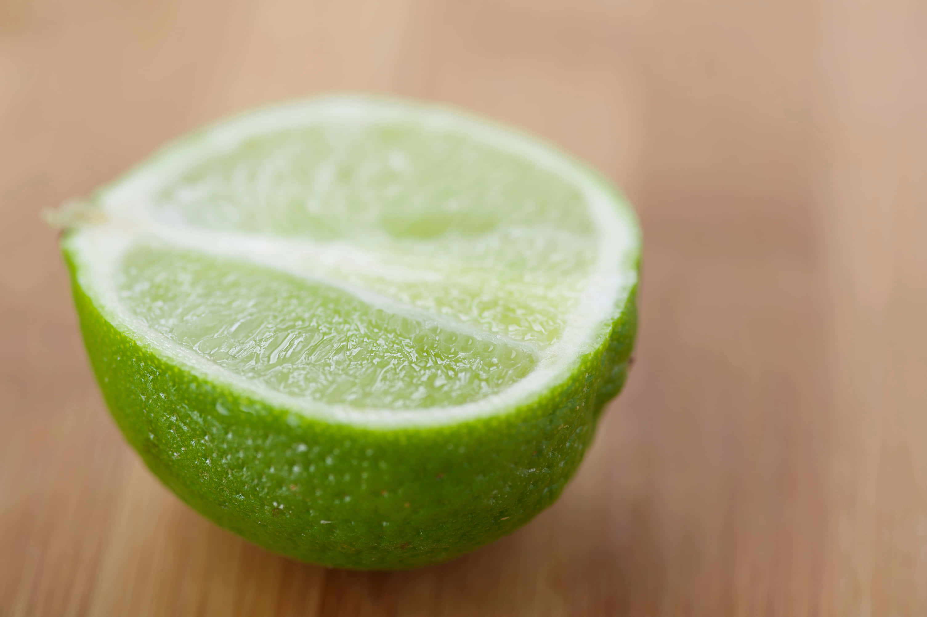 Lime 桌布 壁紙 — 一個充滿活力的綠色萊姆半邊放在溫暖的木質表面上，淺景深突出了其多汁的內部。