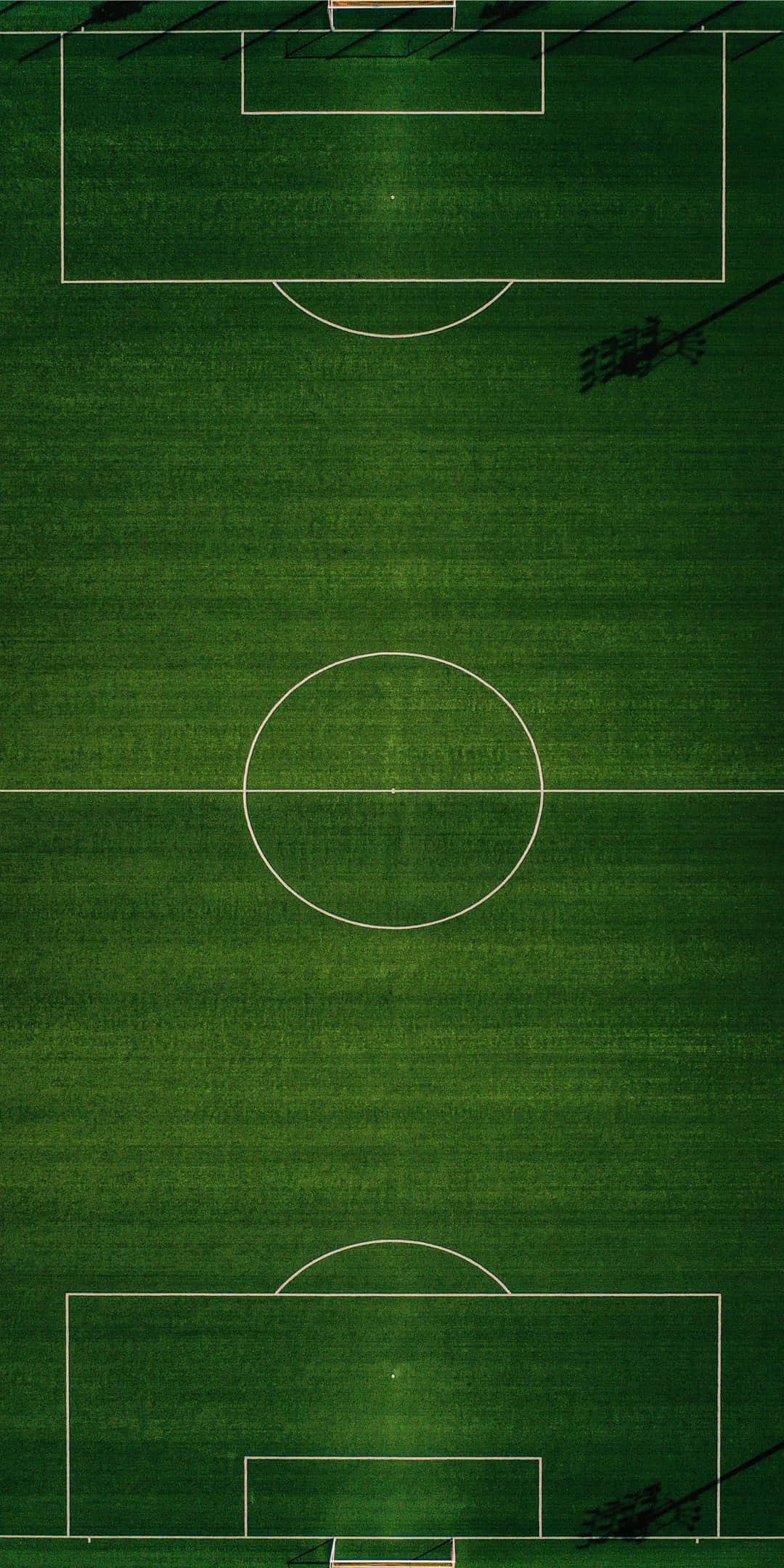 Pixel 3 Sports 桌布 壁紙 — 一個充滿活力的綠色足球場的鳥瞰圖，帶有清晰的白色標記和體育場陰影橫跨球場。