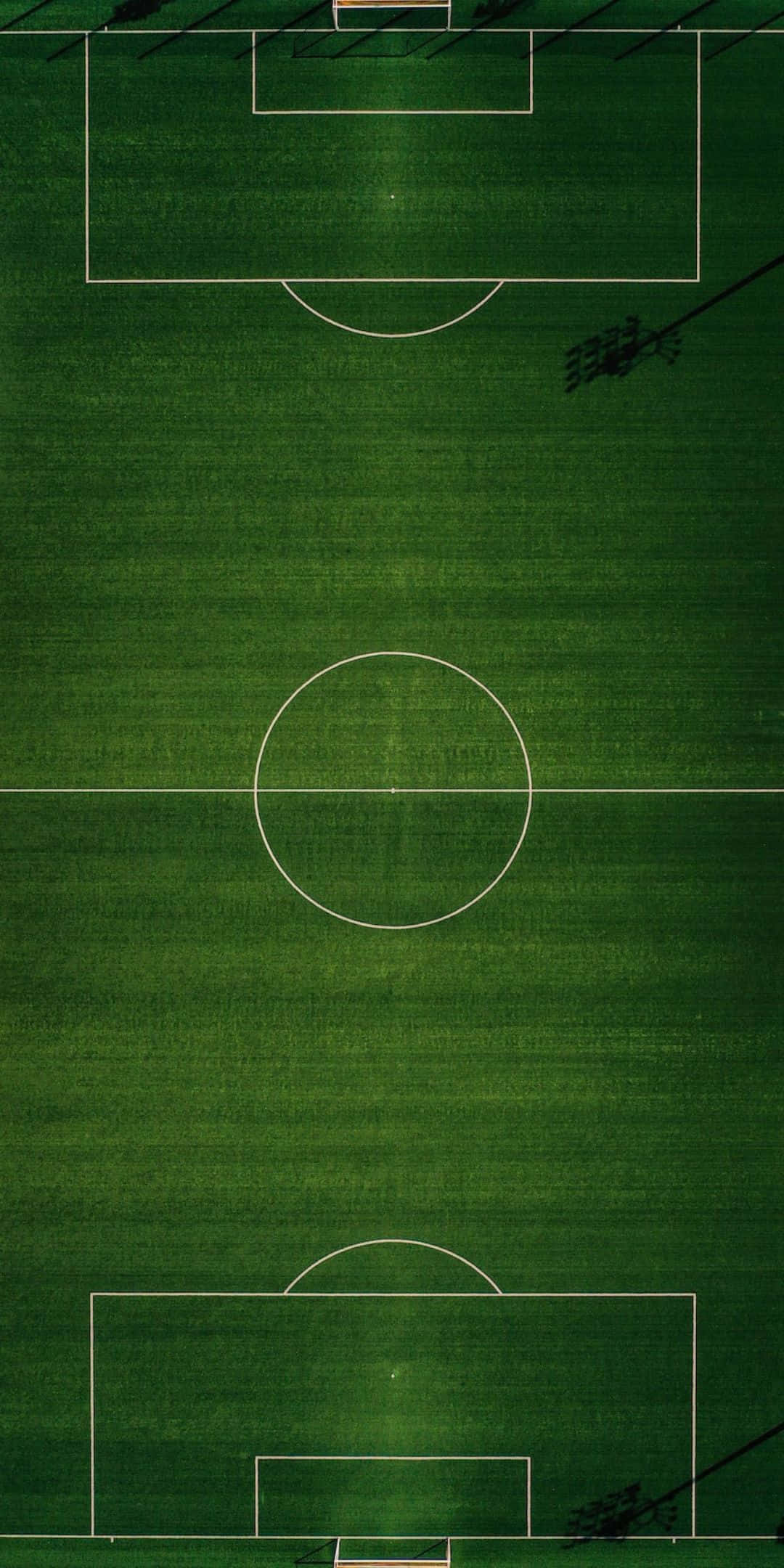Football Field 桌布 壁紙 — 一個充滿活力的綠色足球場的鳥瞰圖，帶有清晰的白色線條和投射陰影的體育場燈光。