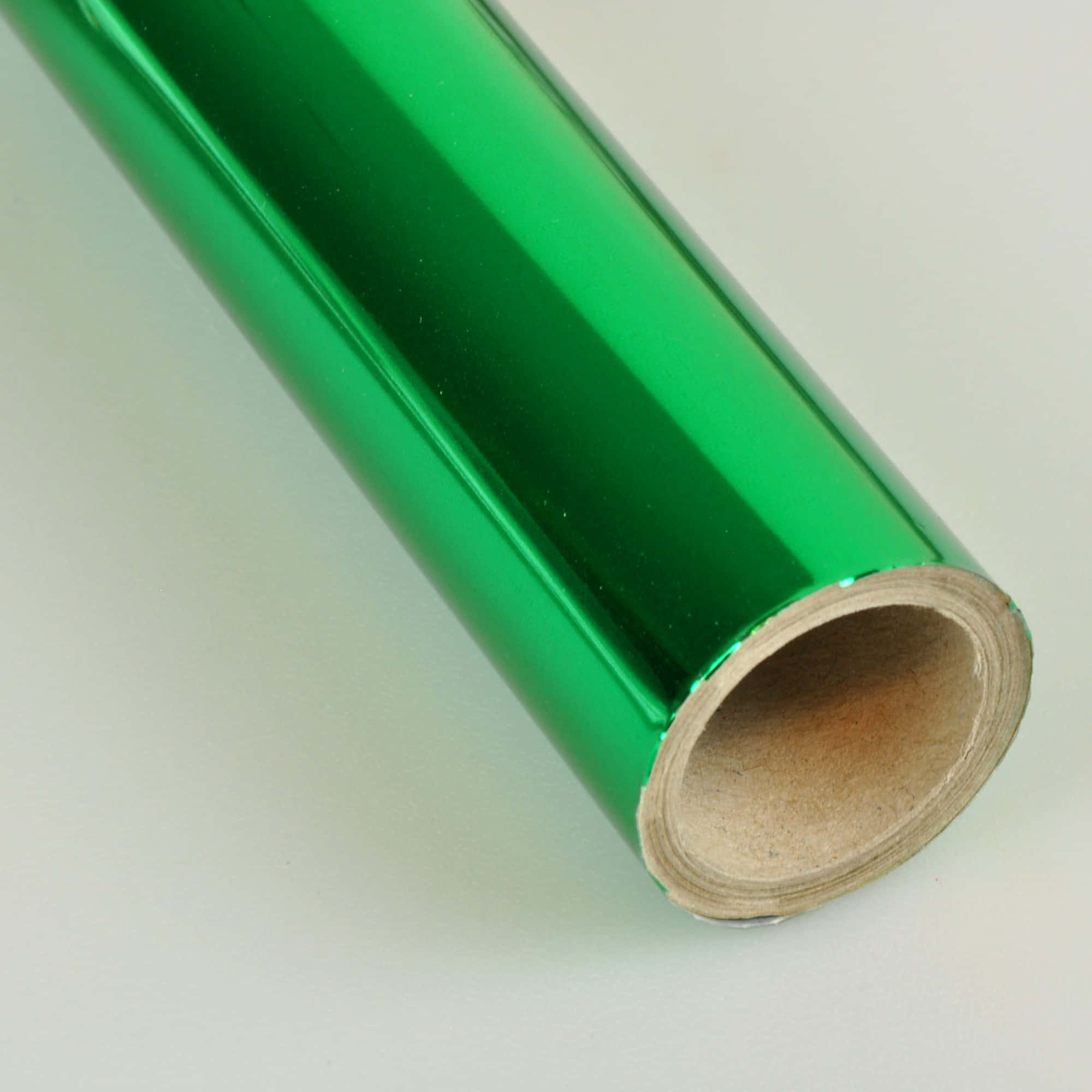 金屬質感 桌布 壁紙 — 一個充滿活力的綠色金屬箔卷，帶有紙板芯，對角放置在純白色表面上。