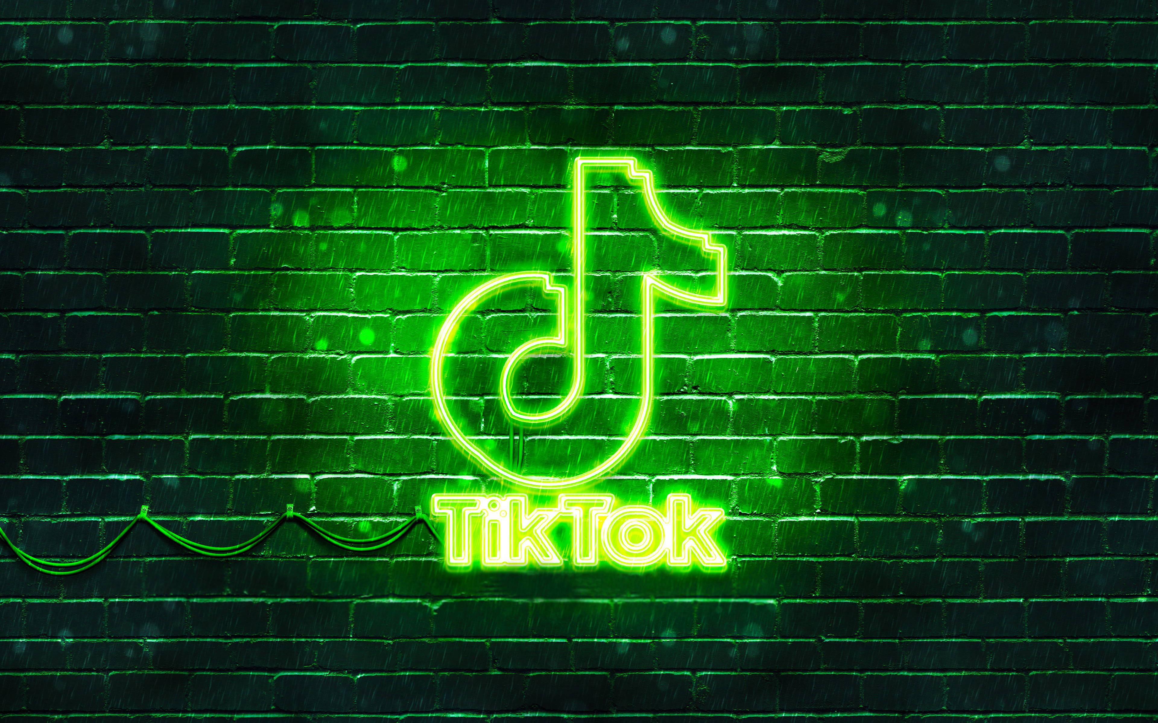 TikTok 動圖 桌布 壁紙 — 一個充滿活力的綠色霓虹燈TikTok標誌在夜雨中對著濕磚牆發光。
