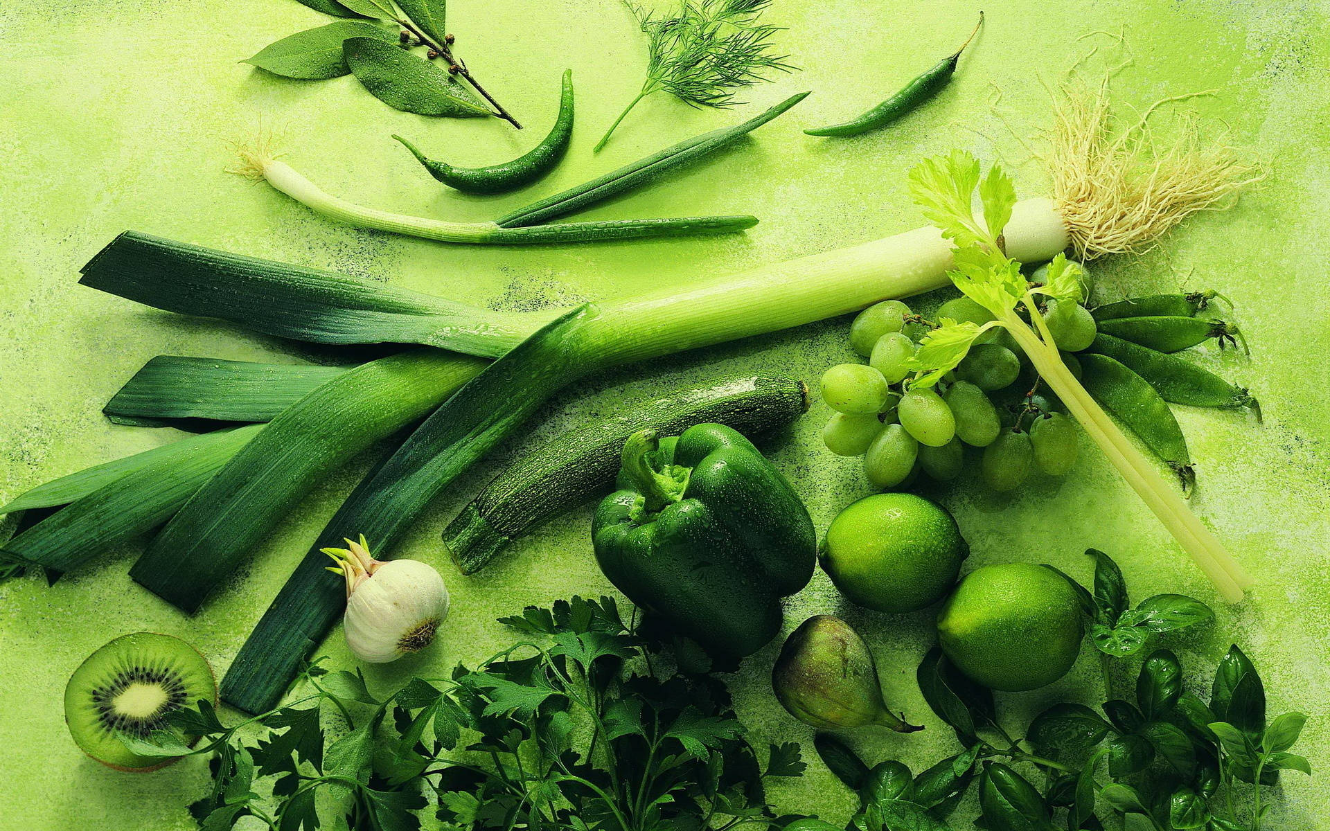 Vegetable 桌布 壁紙 — 一個充滿活力的綠色靜物，新鮮蔬菜、香草和水果排列在帶紋理的綠色表面上。