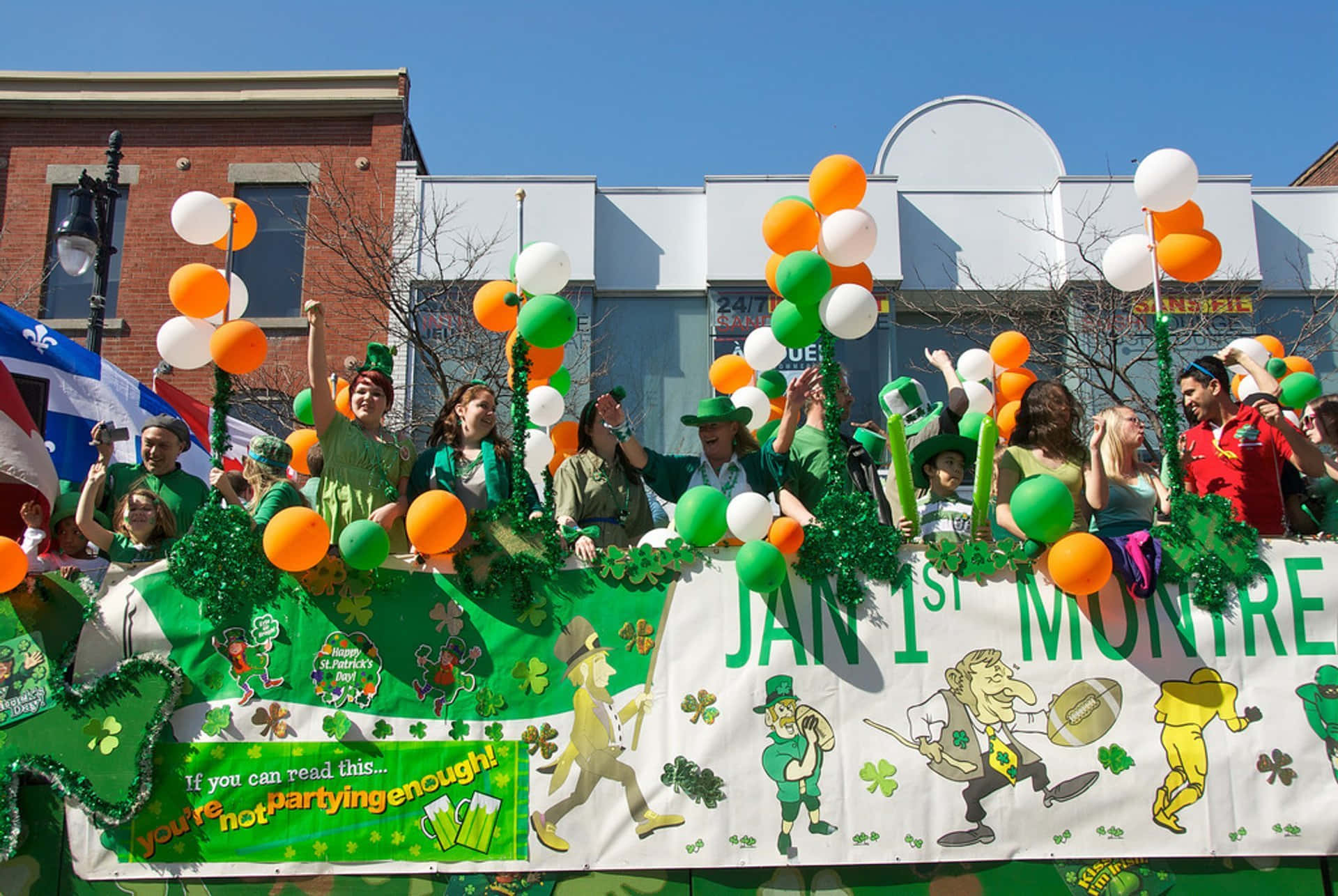 St Patrick's Day 桌布 壁紙 — 一個充滿活力的聖派翠克節遊行花車，人們穿著綠色服裝，在晴朗的藍天下揮舞氣球和歡呼。