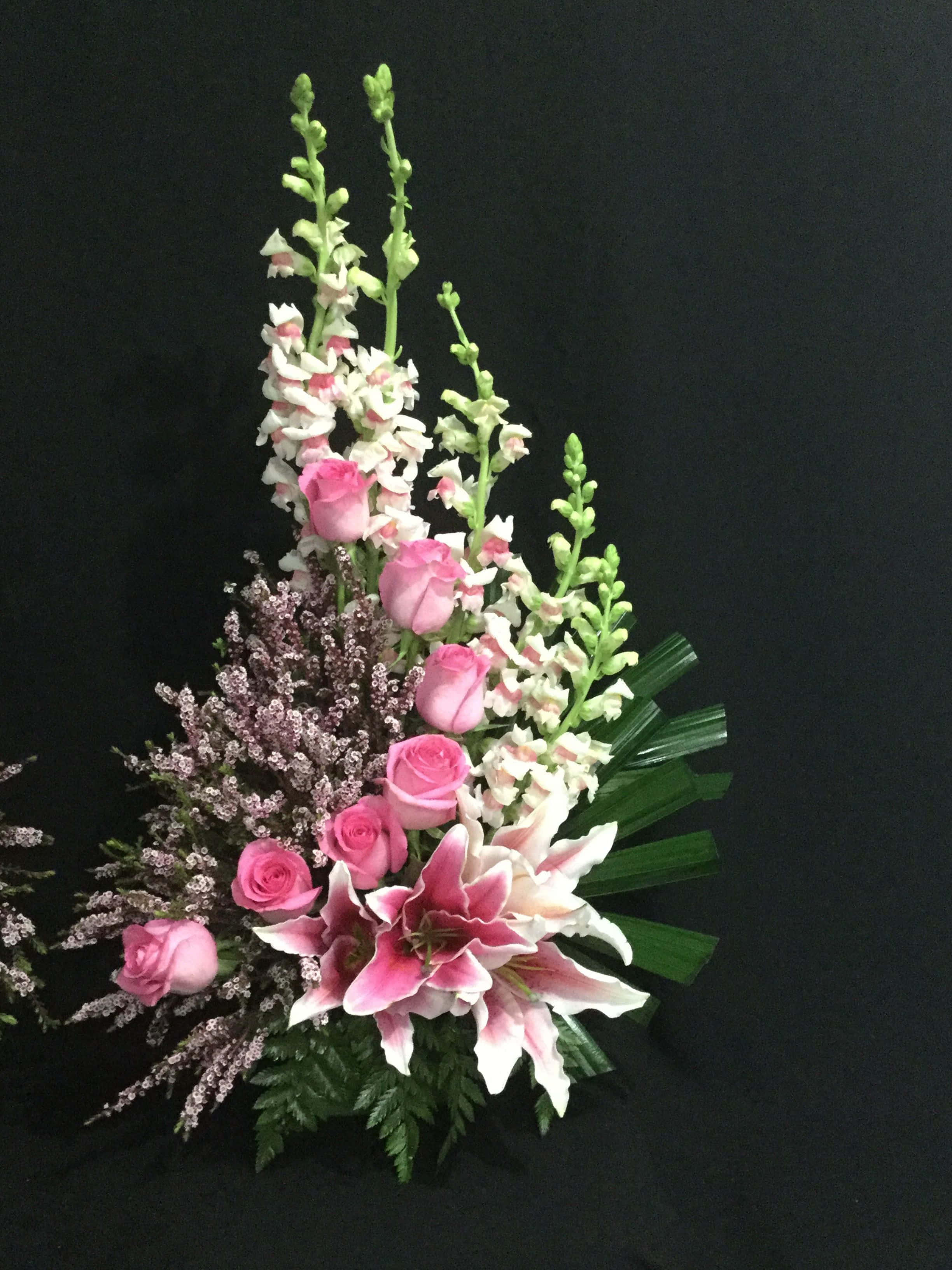 Funeral Flower Arrangements 桌布 壁紙 — 一個充滿活力的花卉佈置，以粉紅玫瑰、百合和毛地黃為特色，襯托在純黑背景上。