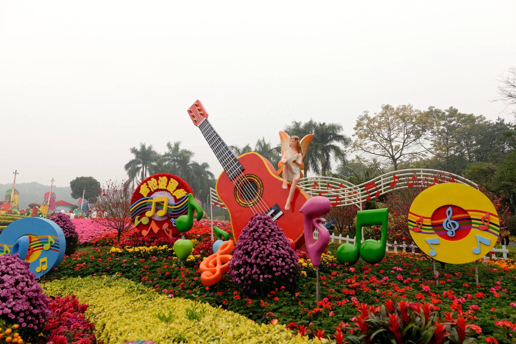 Guangzhou 桌布 壁紙 — 一個充滿活力的花卉展示，特色是巨大的彩色音符和一把紅色吉他，上面棲息著一個小仙女，周圍是盛開的花朵。