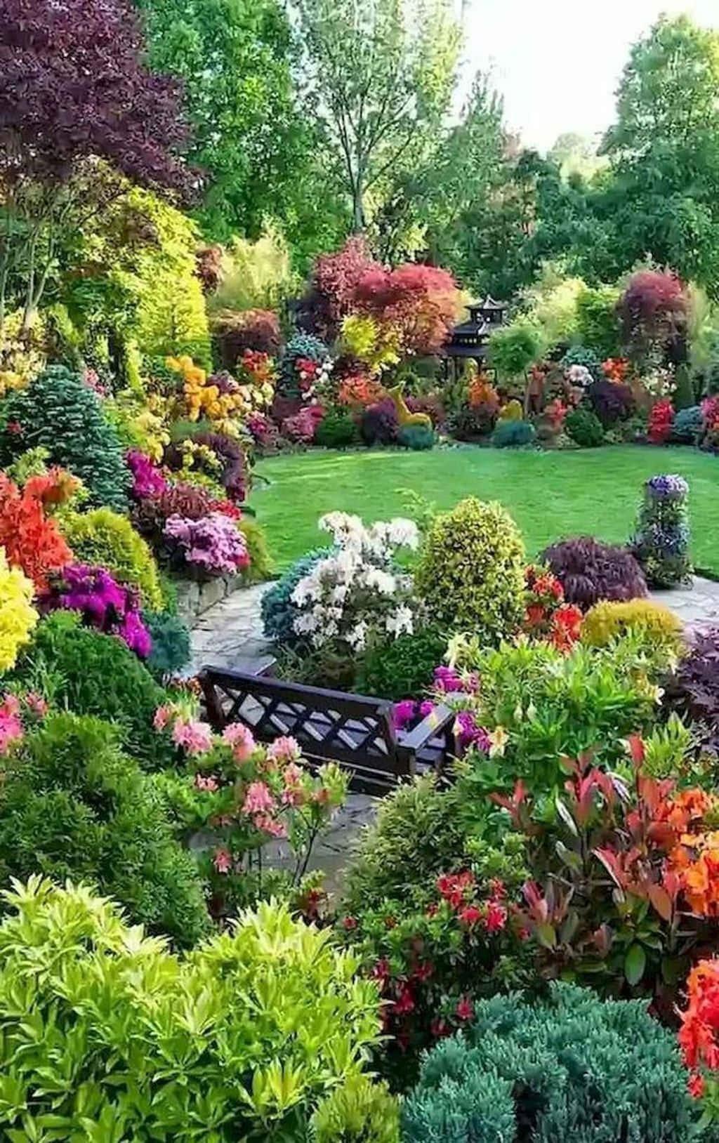 Garden 桌布 壁紙 — 一個充滿活力的花園，開滿了色彩繽紛的花朵和修剪整齊的灌木，環繞著一張在明亮天空下的木製長椅。