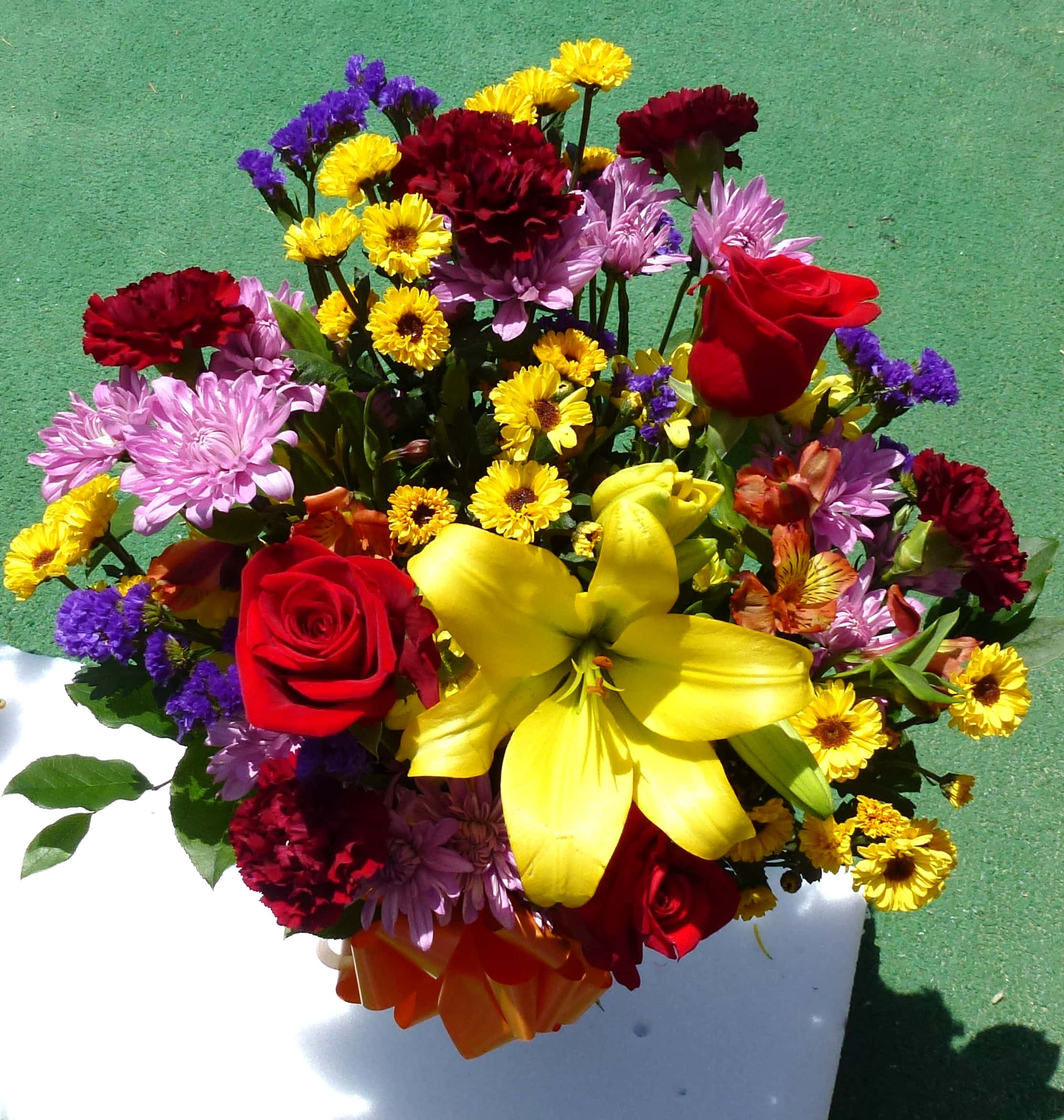 Flower Bouquet 桌布 壁紙 — 一個充滿活力的花束，包含紅玫瑰、黃百合和各種色彩繽紛的花朵，放置在白色容器中，背景為綠色。