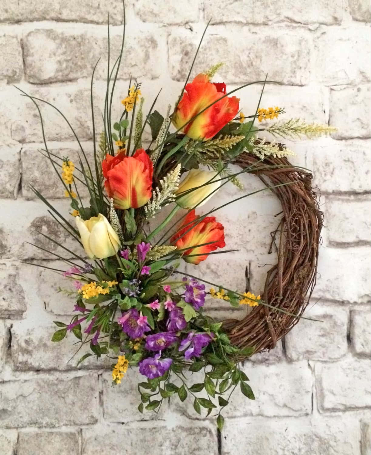 Spring Wreaths 桌布 壁紙 — 一個充滿活力的花環，帶有紅色、黃色和紫色的花朵，掛在白色磚牆上。