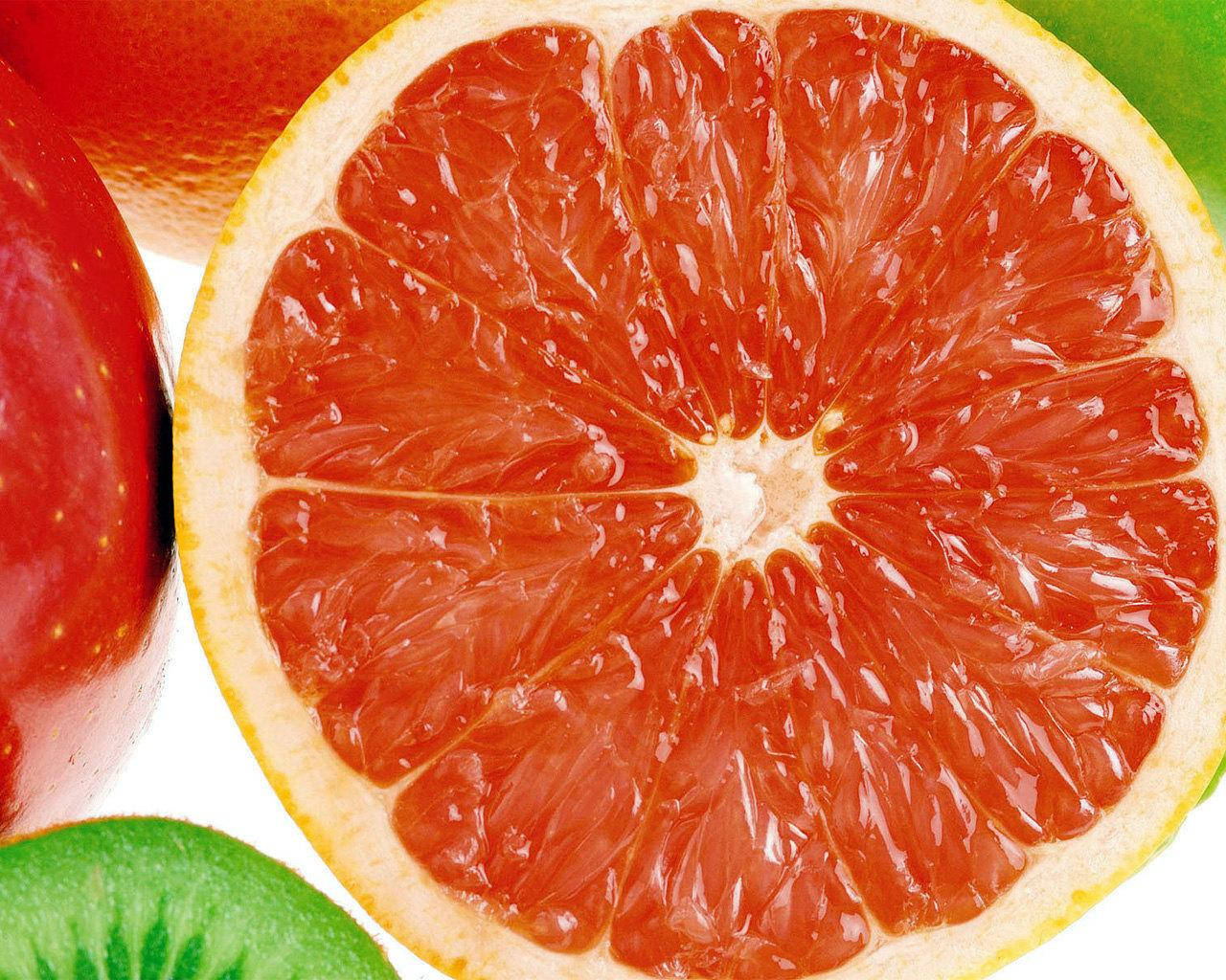 Grapefruit 桌布 壁紙 — 一個充滿活力的葡萄柚切片特寫，露出多汁的紅色果肉，旁邊有紅蘋果和綠色奇異果切片。