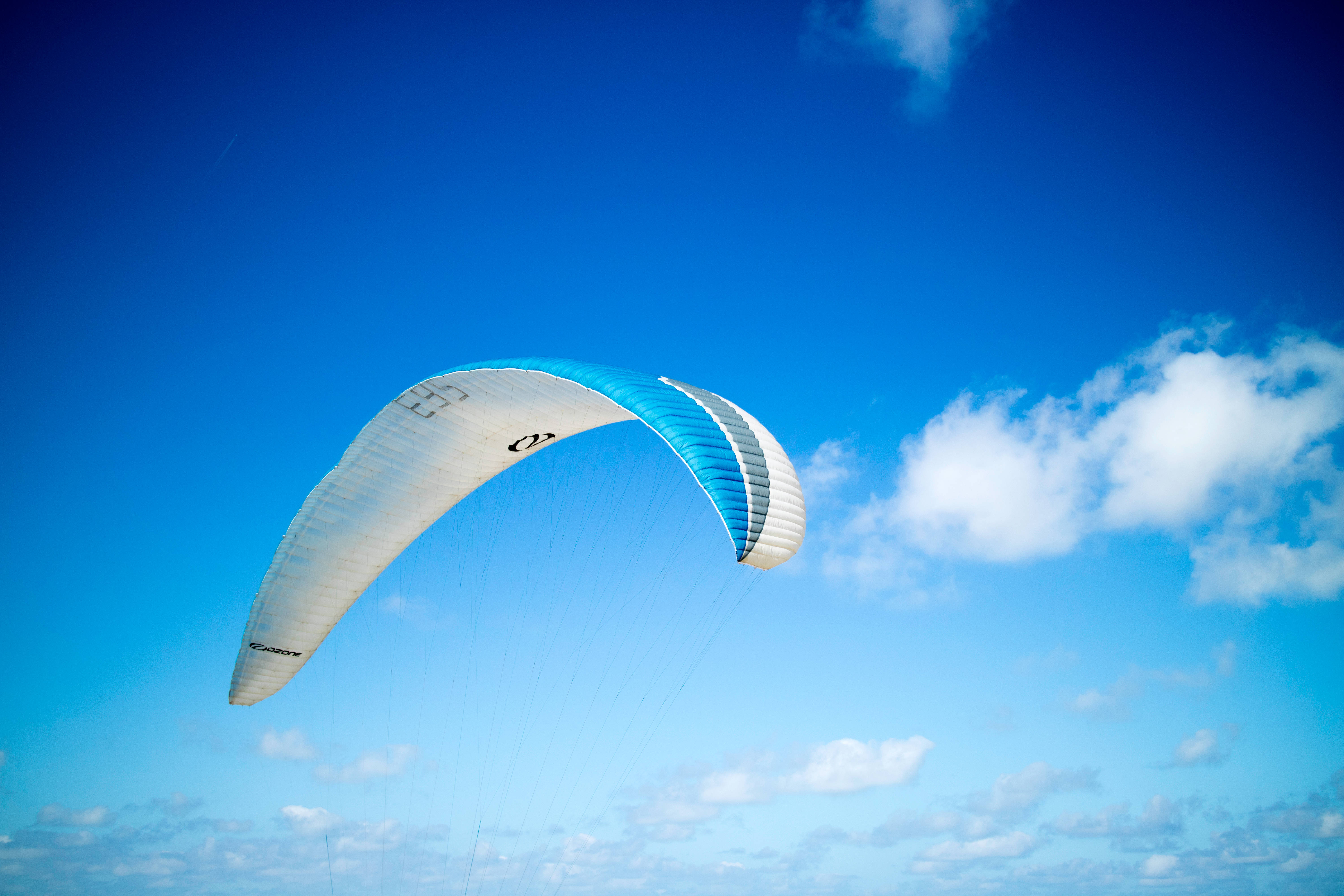 Paragliding 桌布 壁紙 — 一個充滿活力的藍白相間滑翔傘在點綴著蓬鬆白雲的清澈藍天中優雅翱翔。