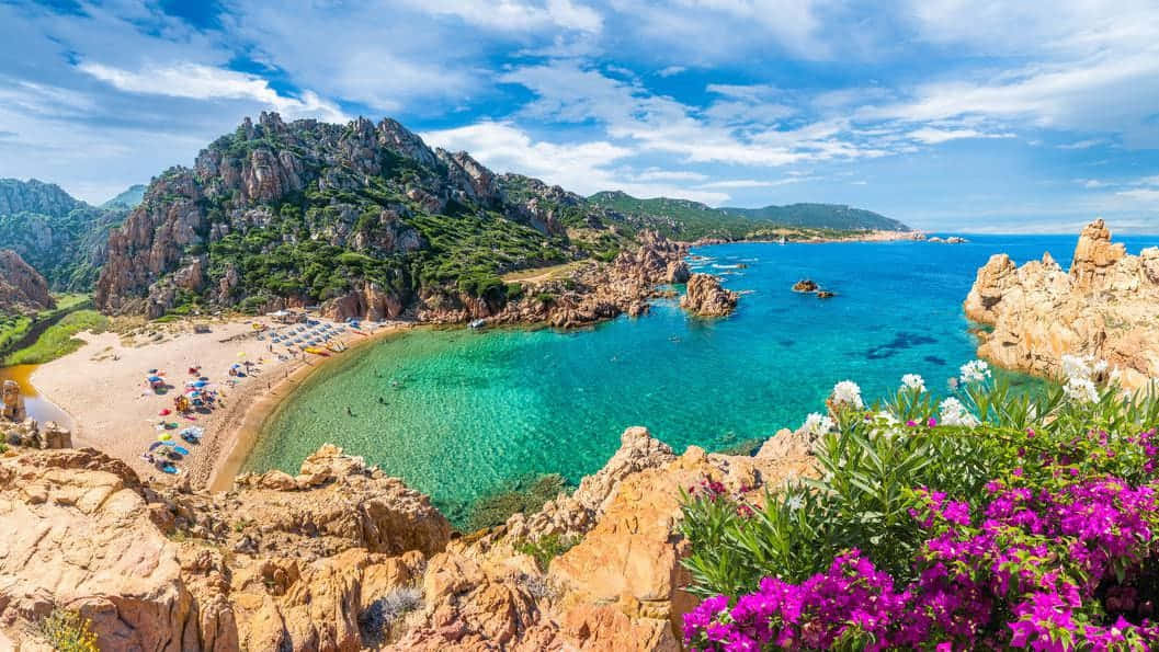 Italian Island 桌布 壁紙 — 一個充滿活力的藍綠色海灣，坐落在崎嶇的懸崖之間，沙灘上點綴著色彩繽紛的遮陽傘，天空湛藍明亮。