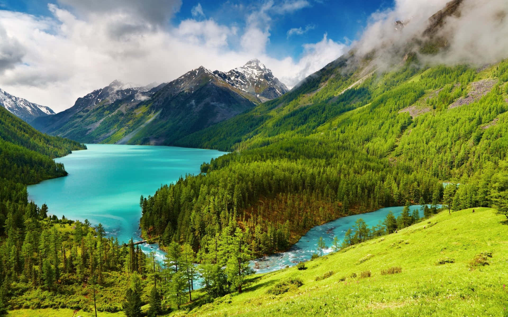 screensaver 桌布 壁紙 — 一個充滿活力的藍綠色湖泊，坐落在鬱鬱蔥蔥的綠色山脈中，山頂積雪，天空多雲。