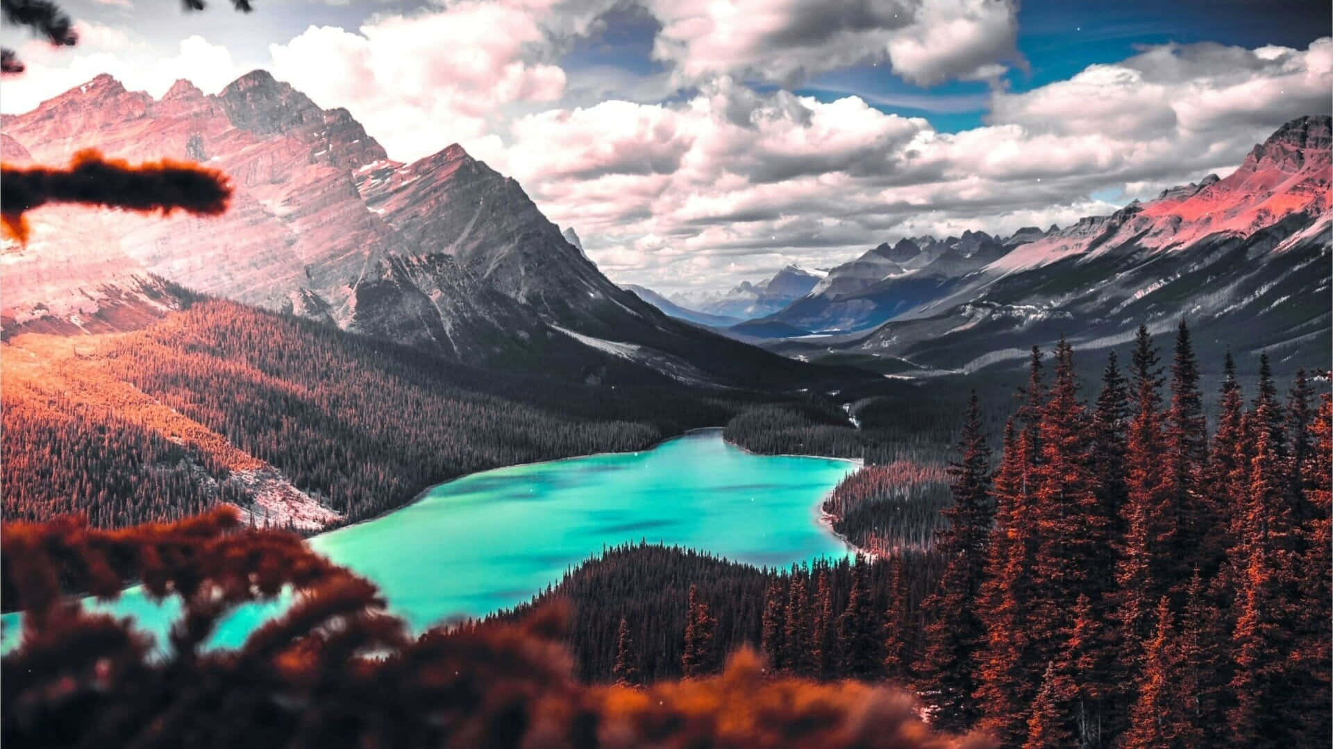山景 桌布 壁紙 — 一個充滿活力的藍綠色湖泊，坐落在高聳的山脈之間，天空佈滿戲劇性的雲層，前景是秋天的樹木。