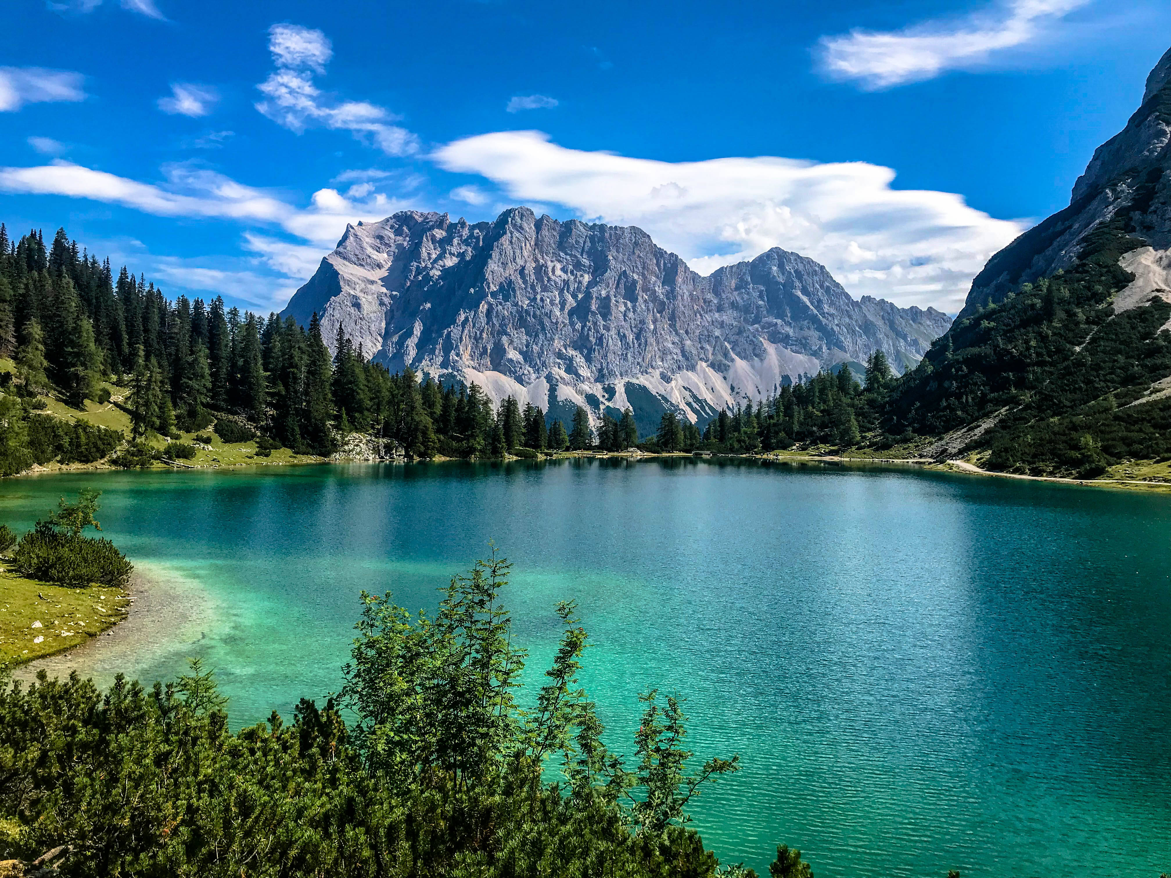 Lake 桌布 壁紙 — 一個充滿活力的藍綠色湖泊映照著鋸齒狀的山脈，天空湛藍，雲朵稀疏。