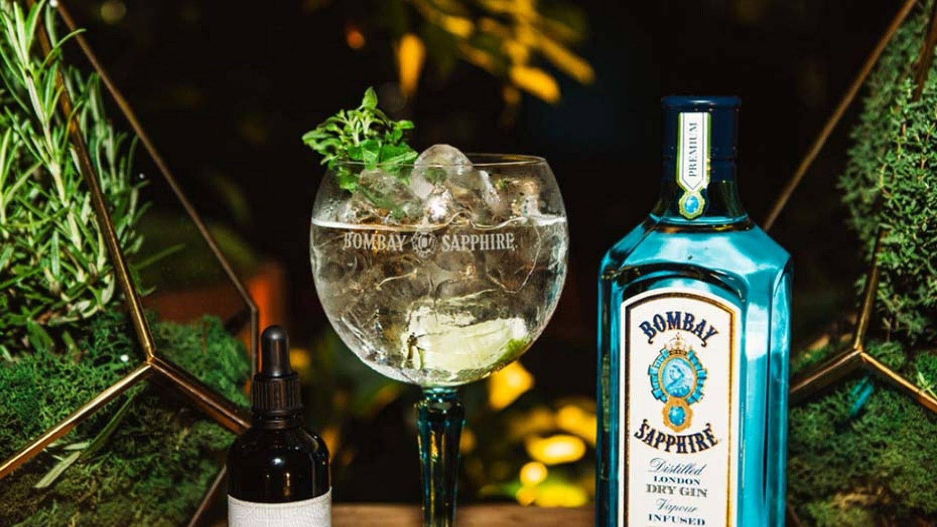 Wine 桌布 壁紙 — 一個充滿活力的藍色 Bombay Sapphire 琴酒瓶旁邊放著一杯加冰、用香草裝飾的琴酒雞尾酒。