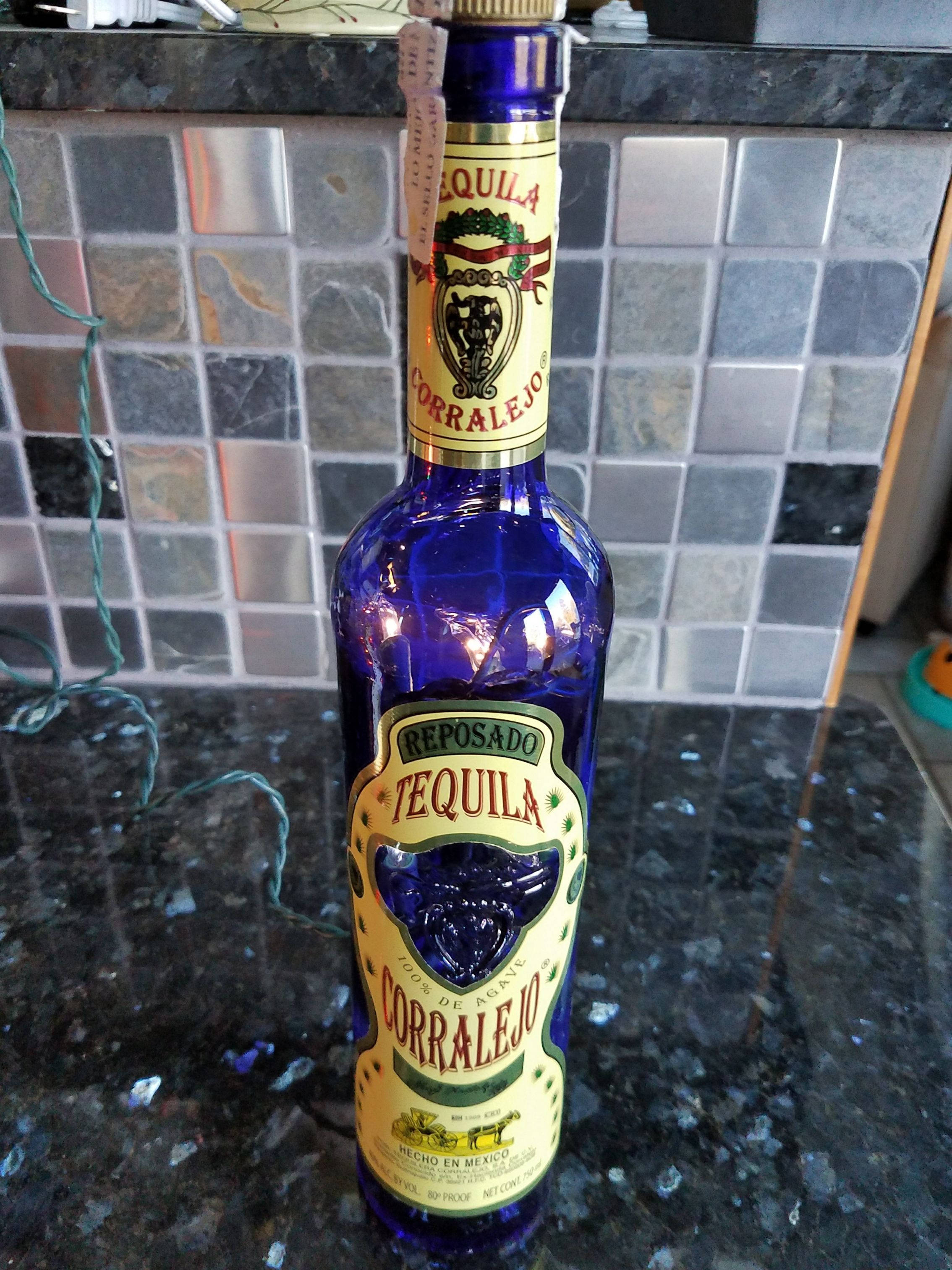 Drink 桌布 壁紙 — 一個充滿活力的藍色Corralejo reposado龍舌蘭酒瓶在深色花崗岩檯面上閃閃發光，背景是馬賽克瓷磚防濺板。