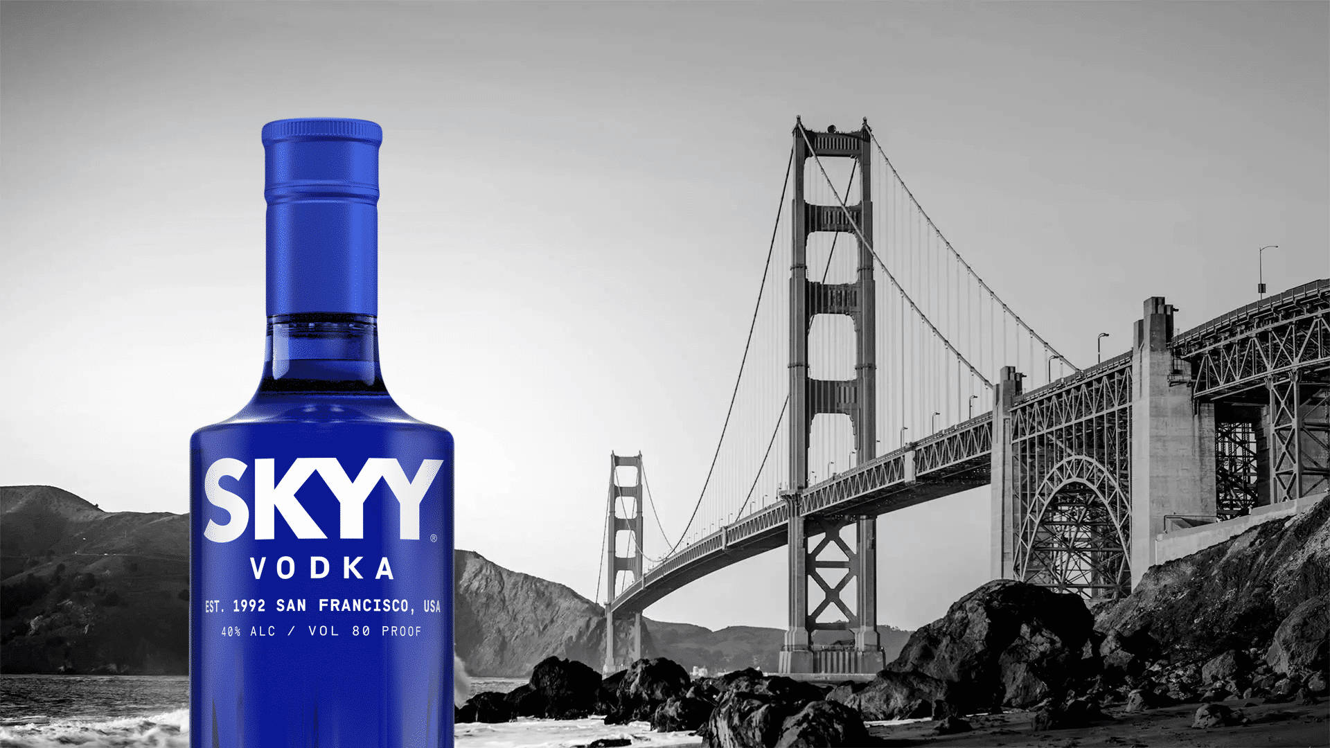 藍色 桌布 壁紙 — 一個充滿活力的藍色Skyy伏特加酒瓶矗立在黑白金門大橋背景的前景中。