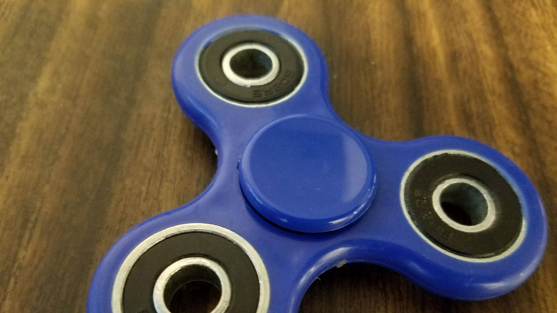 toys 桌布 壁紙 — 一個充滿活力的藍色指尖陀螺放在溫暖的木質表面上，木紋清晰可見。