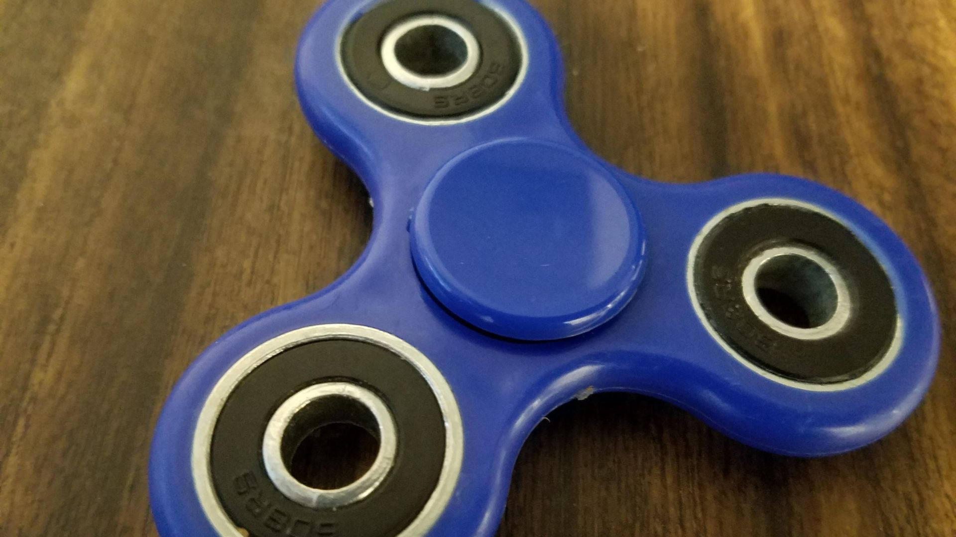 toys 桌布 壁紙 — 一個充滿活力的藍色指尖陀螺放在溫暖的木質表面上，木紋清晰可見。