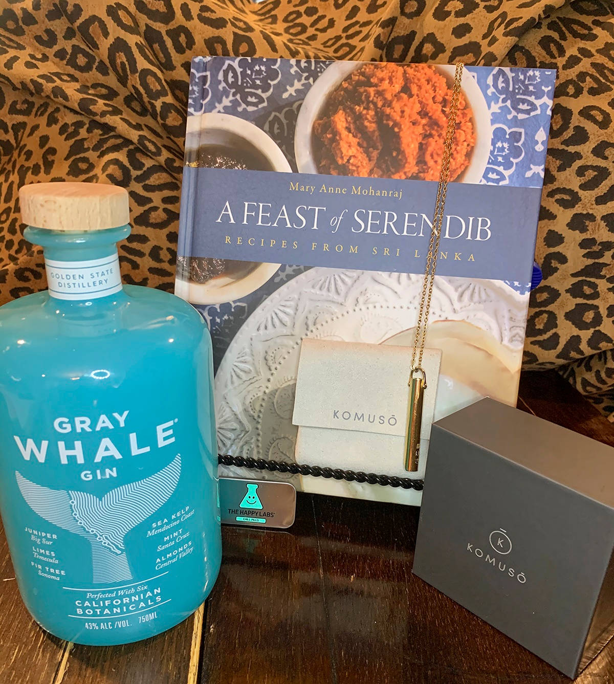 鯨魚 桌布 壁紙 — 一個充滿活力的藍色琴酒瓶旁邊放著一本斯里蘭卡食譜和奢華珠寶，背景是豹紋圖案。