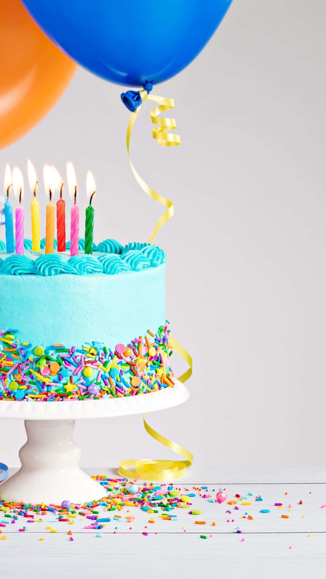 Birthday Cake 桌布 壁紙 — 一個充滿活力的藍色生日蛋糕，上面有燃燒的蠟燭和彩色糖粒，放在白色支架上，旁邊有漂浮的氣球。