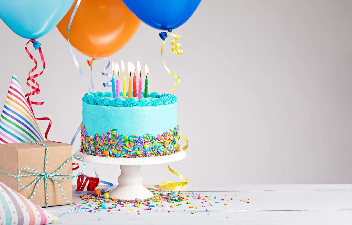 Birthday 桌布 壁紙 — 一個充滿活力的藍色生日蛋糕，上面有燃燒的蠟燭和彩色糖粒，旁邊放著氣球和一個禮物盒，放在白色木桌上。