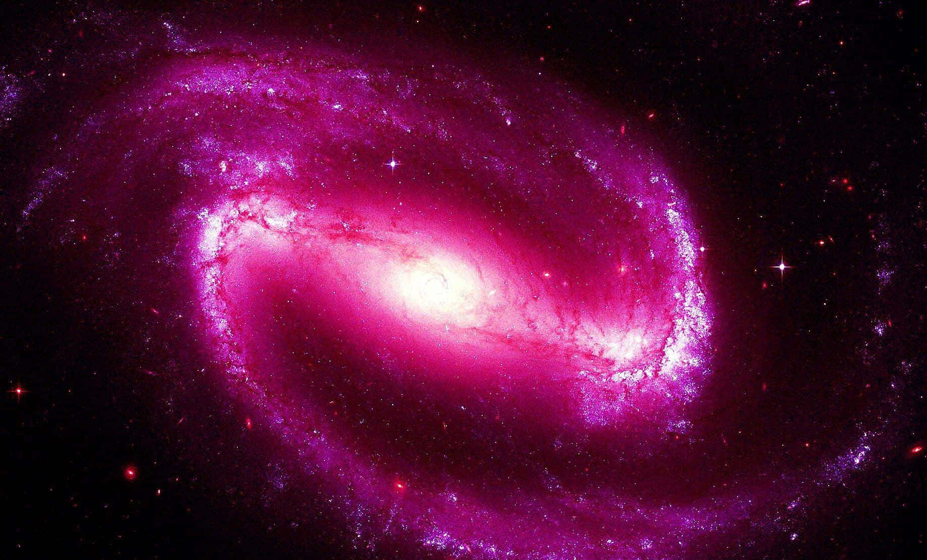 粉紅銀河 桌布 壁紙 — 一個充滿活力的螺旋星系在佈滿星點的宇宙虛空中散發出洋紅色和粉紅色的光芒。