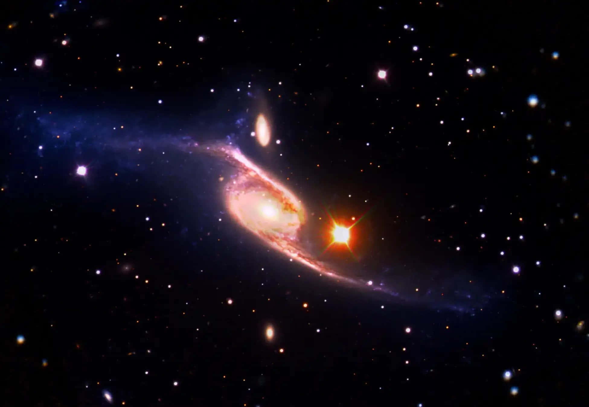 Nasa Galaxy 桌布 壁紙 — 一個充滿活力的螺旋星系在星場中旋轉，呈現粉紅色和藍色色調，並被明亮的橙色星爆照亮。