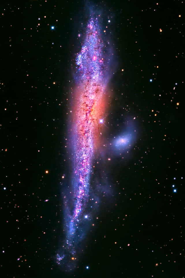 Elliptical Galaxy 桌布 壁紙 — 一個充滿活力的螺旋星系在深空的星場中散發出紫色、粉紅色和橙色的色調。