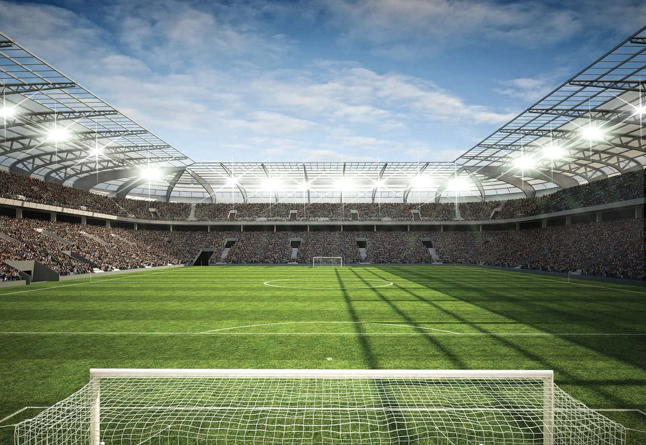Soccer Stadium 桌布 壁紙 — 一個充滿活力的足球場，在明亮的燈光和晴朗的藍天下擠滿了歡呼的球迷。