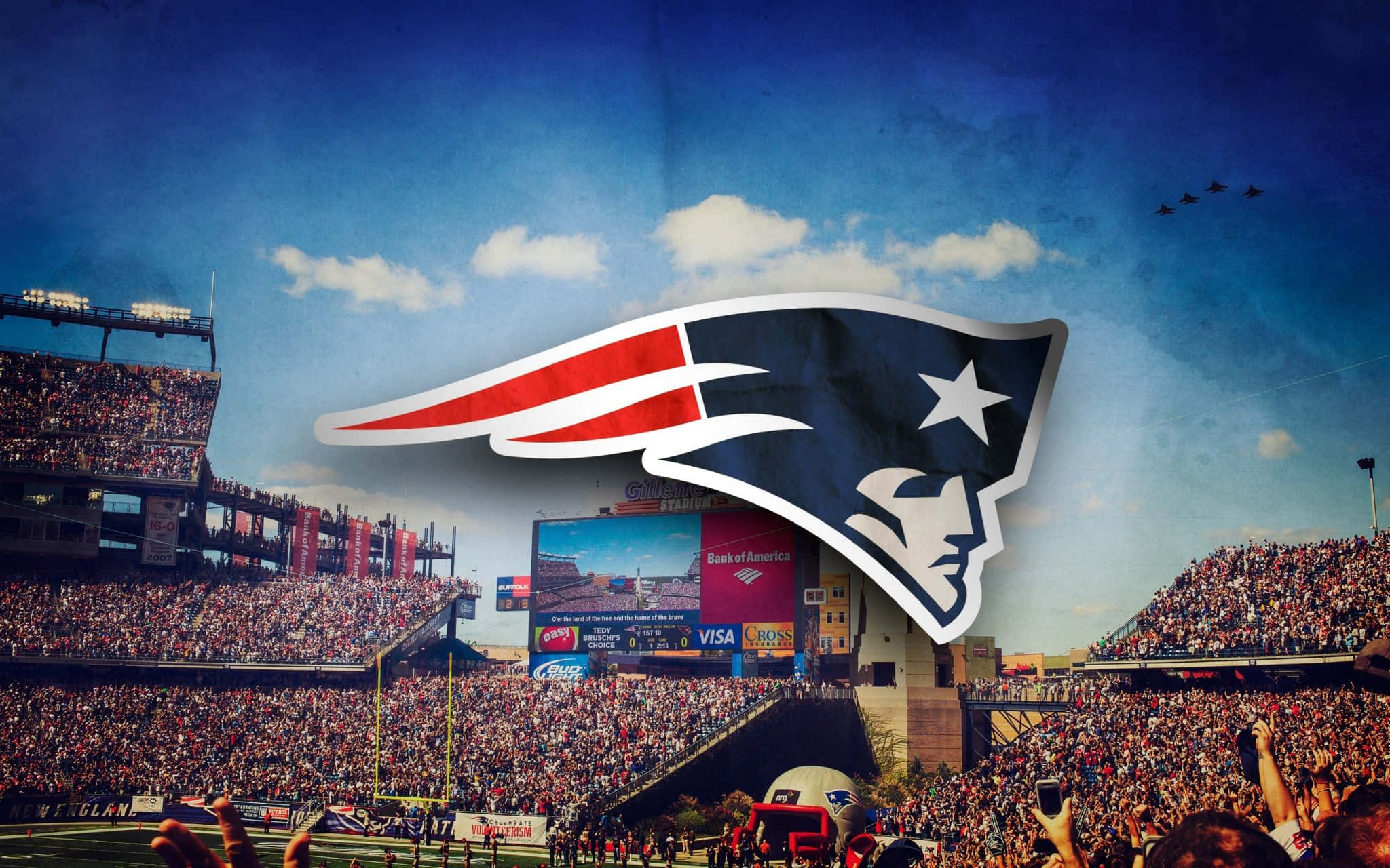 Patriots 桌布 壁紙 — 一個充滿活力的足球場，擠滿了歡呼的球迷，藍天下覆蓋著一個大型新英格蘭愛國者隊標誌。