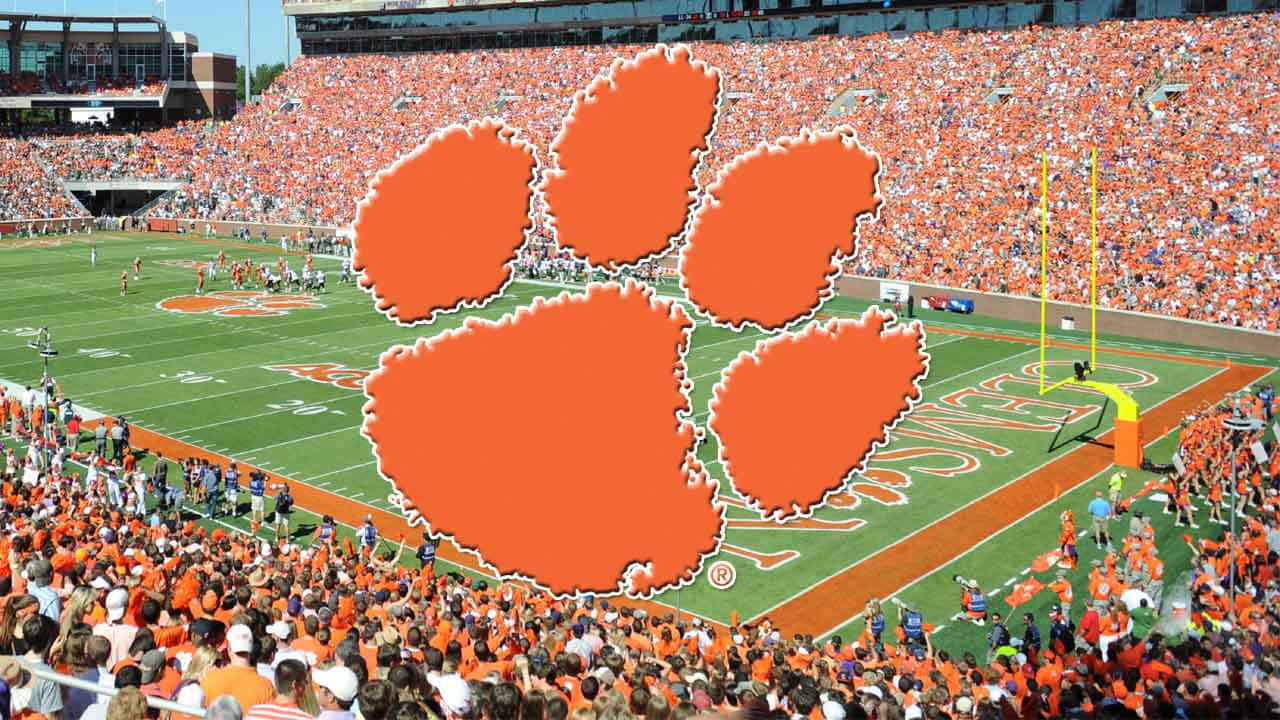 Clemson 桌布 壁紙 — 一個充滿活力的足球場，擠滿了身穿橙色衣服的球迷，在比賽中歡呼，並有巨大的爪子標誌覆蓋。
