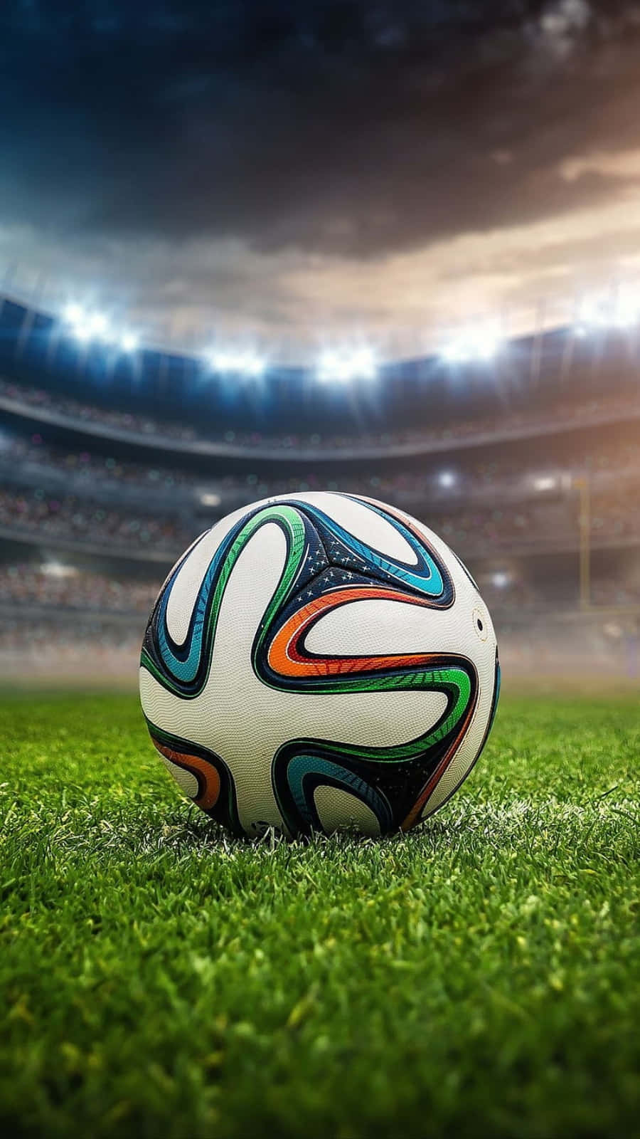 Soccer Ball 桌布 壁紙 — 一個充滿活力的足球放在茂密的綠草上，球場燈光下，天空多雲而戲劇化。
