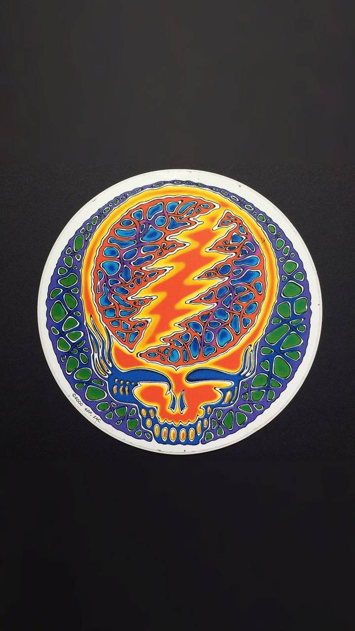 dead 桌布 壁紙 — 一個充滿活力的迷幻骷髏，眼睛穿過閃電，周圍是綠色和藍色馬賽克圖案，背景為黑色。