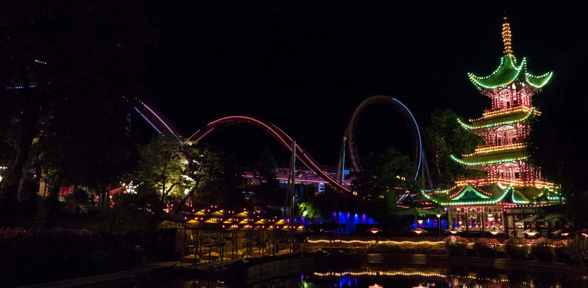 Park 桌布 壁紙 — 一個充滿活力的遊樂園夜景，特色是發光的寶塔和明亮的雲霄飛車，映襯著黑暗的天空。