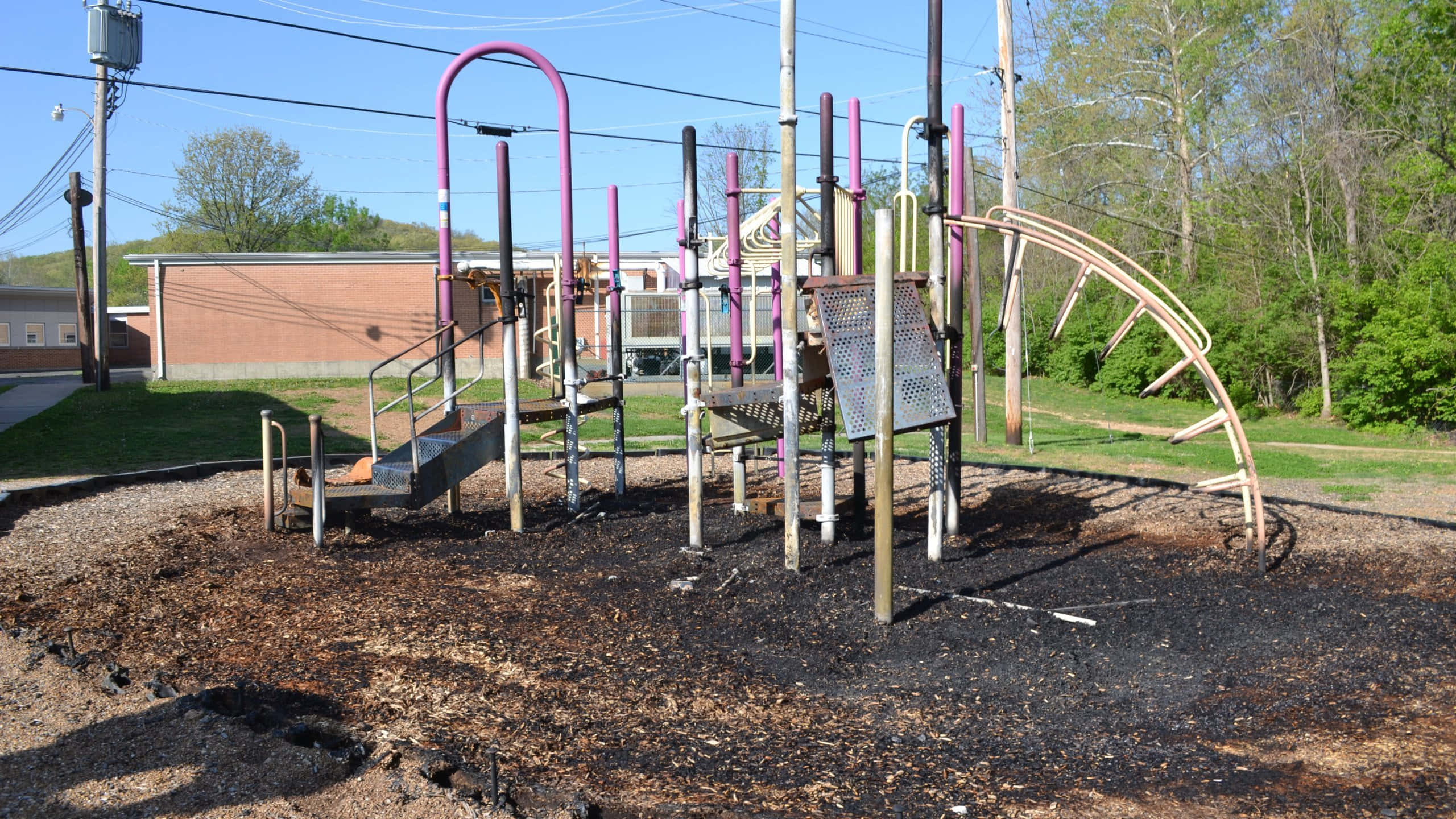 Playground 桌布 壁紙 — 一個充滿活力的遊樂場，紫色和米色的結構矗立在深色覆蓋物上，在晴朗的藍天下。