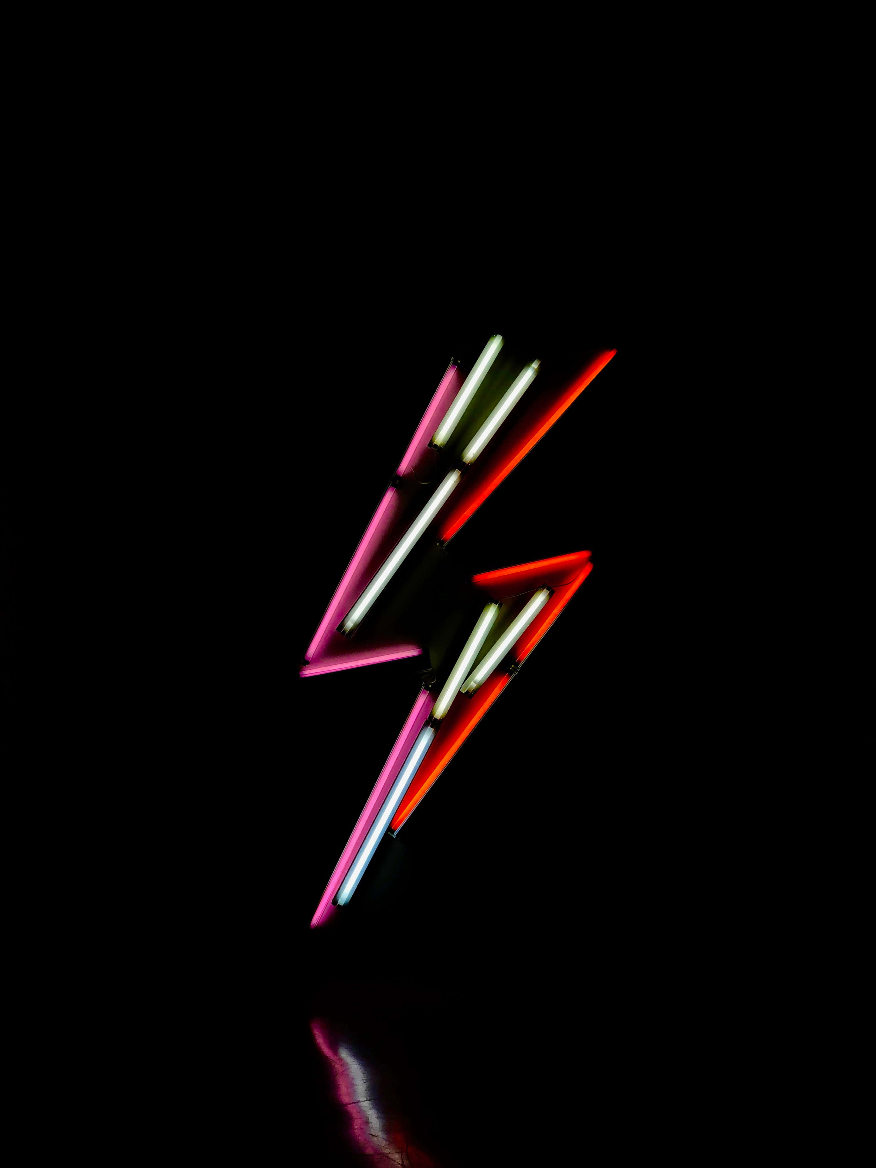 Neon Lightning 桌布 壁紙 — 一個充滿活力的霓虹閃電雕塑，在漆黑背景上發出粉紅、紅色和白色的光芒。