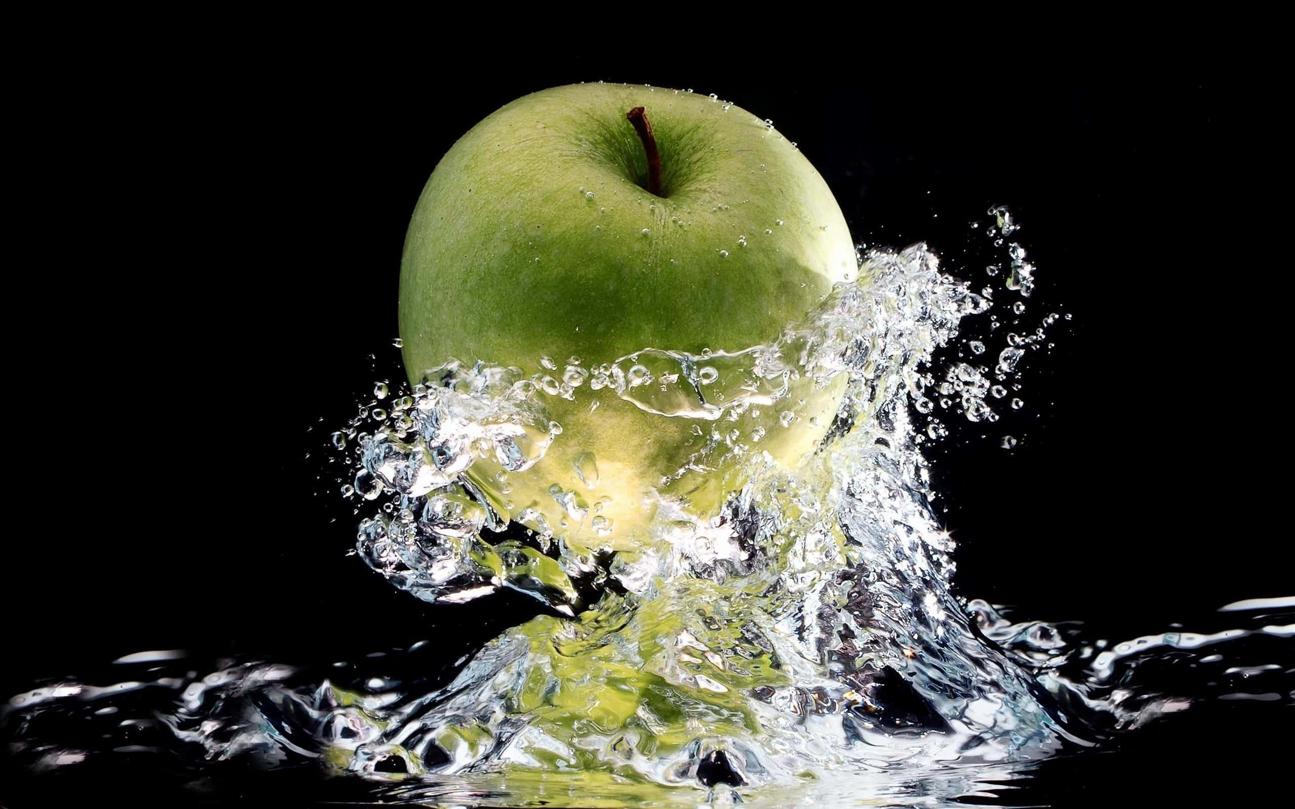 Refreshing 桌布 壁紙 — 一個充滿活力的青蘋果在清澈的水中戲劇性地飛濺，背景是純黑色。