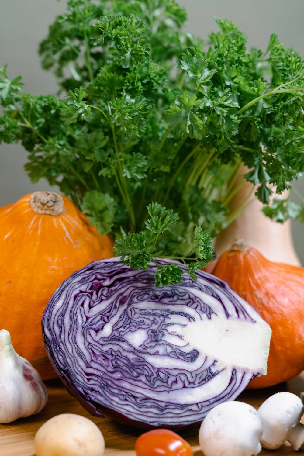 Vegetables 桌布 壁紙 — 一個充滿活力的靜物畫，包括切片紅椰菜、歐芹、南瓜、大蒜、蘑菇和櫻桃番茄，排列在木質表面上。