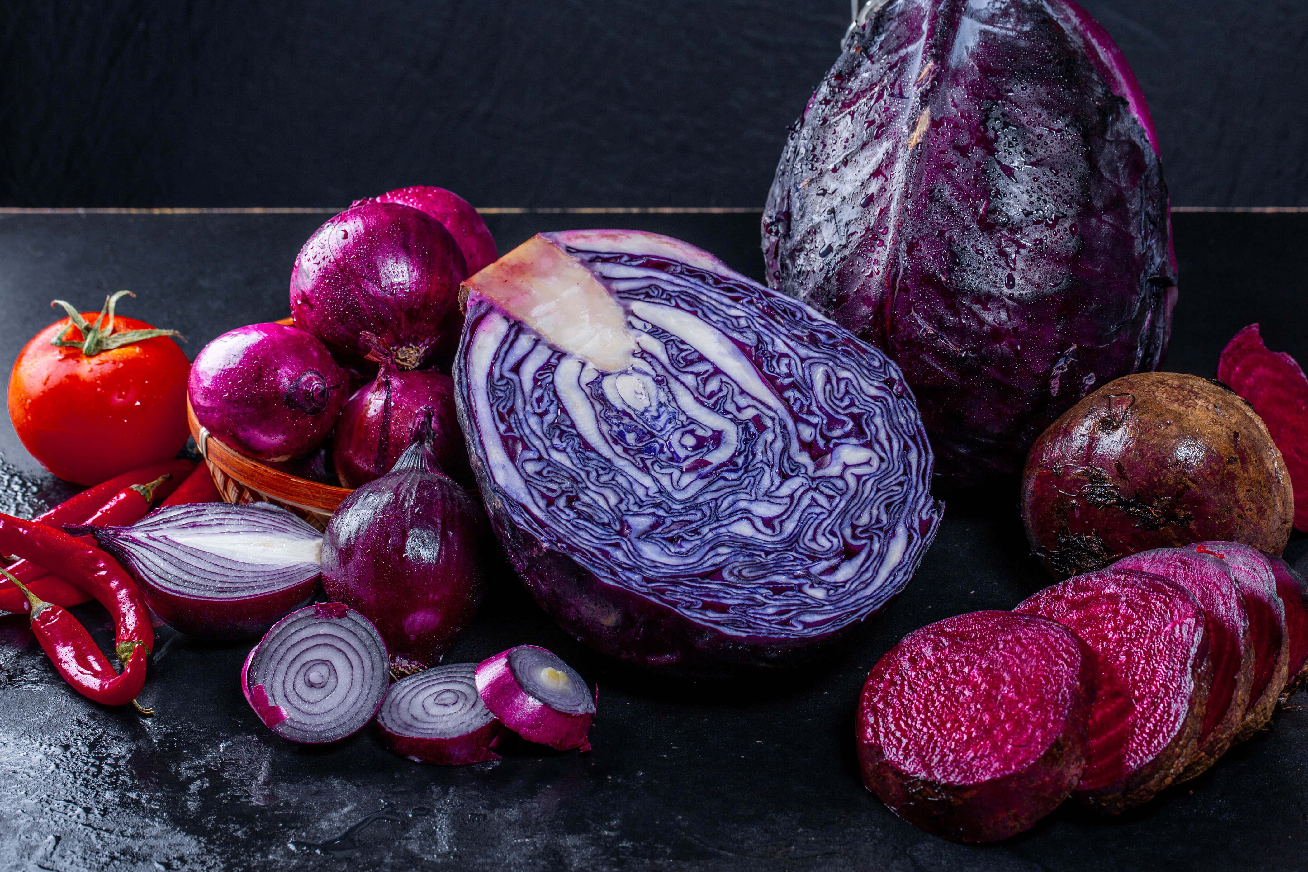 Purple Onions 桌布 壁紙 — 一個充滿活力的靜物畫，展示了切片紅高麗菜、甜菜根、小番茄和紅洋蔥，排列在深色紋理表面上。