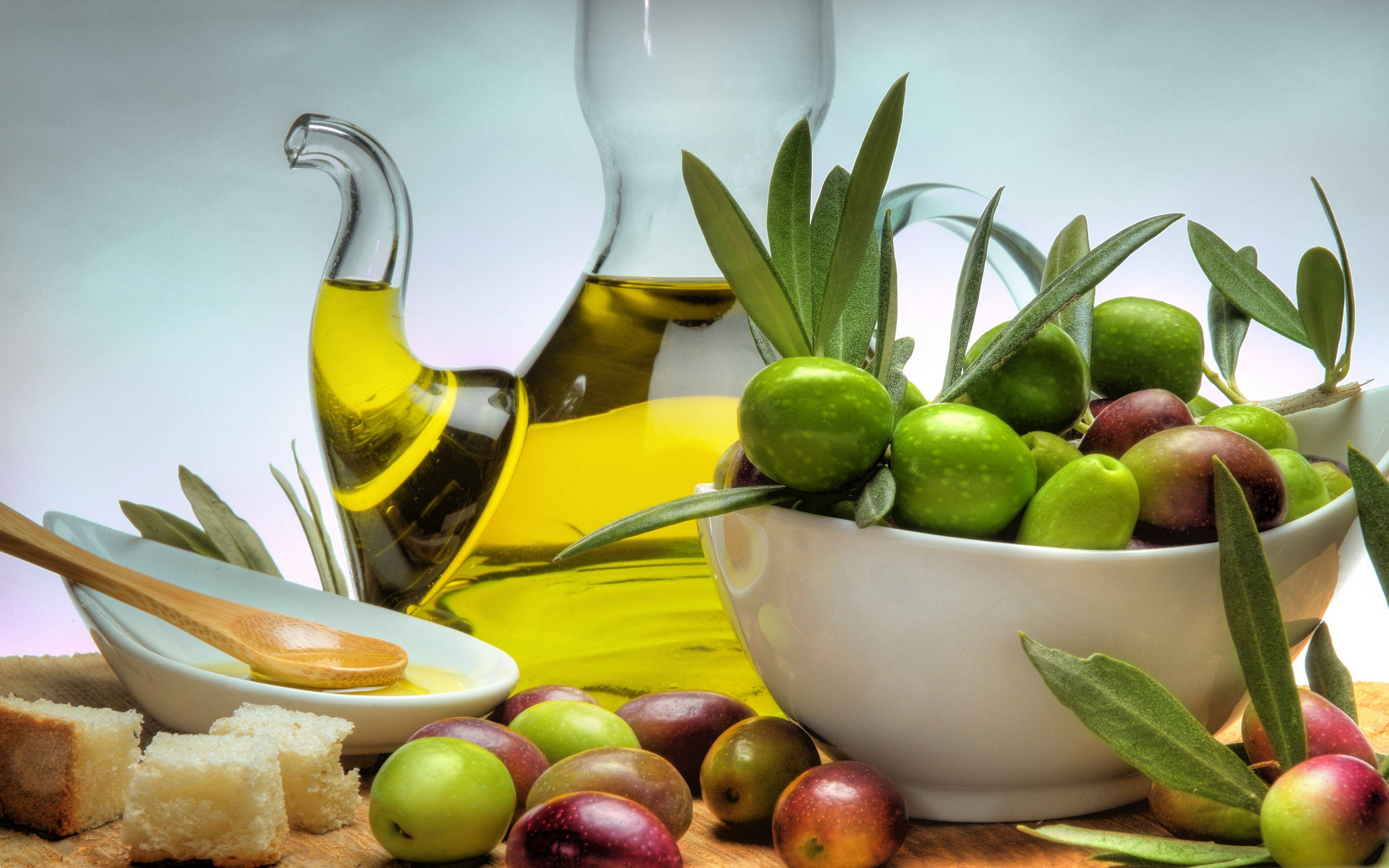 Fruits 桌布 壁紙 — 一個充滿活力的靜物畫，展示白色碗中的新鮮綠色和紫色橄欖，旁邊是一個裝有金色橄欖油的玻璃瓶和麵包塊。