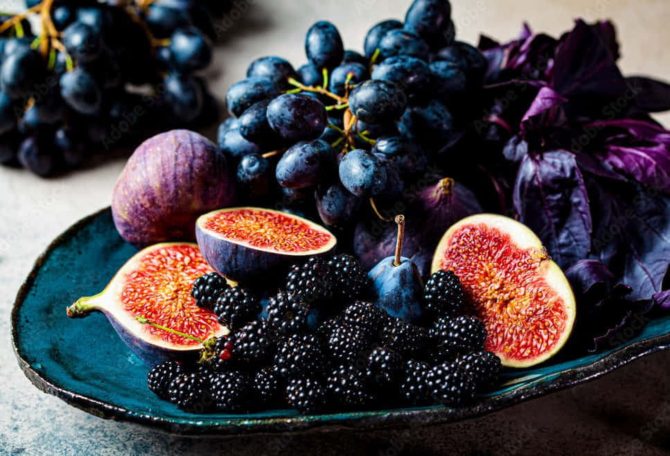 Fruits 桌布 壁紙 — 一個充滿活力的靜物畫，深色葡萄、無花果和黑莓排列在青綠色盤子上，配以紫色羅勒葉。