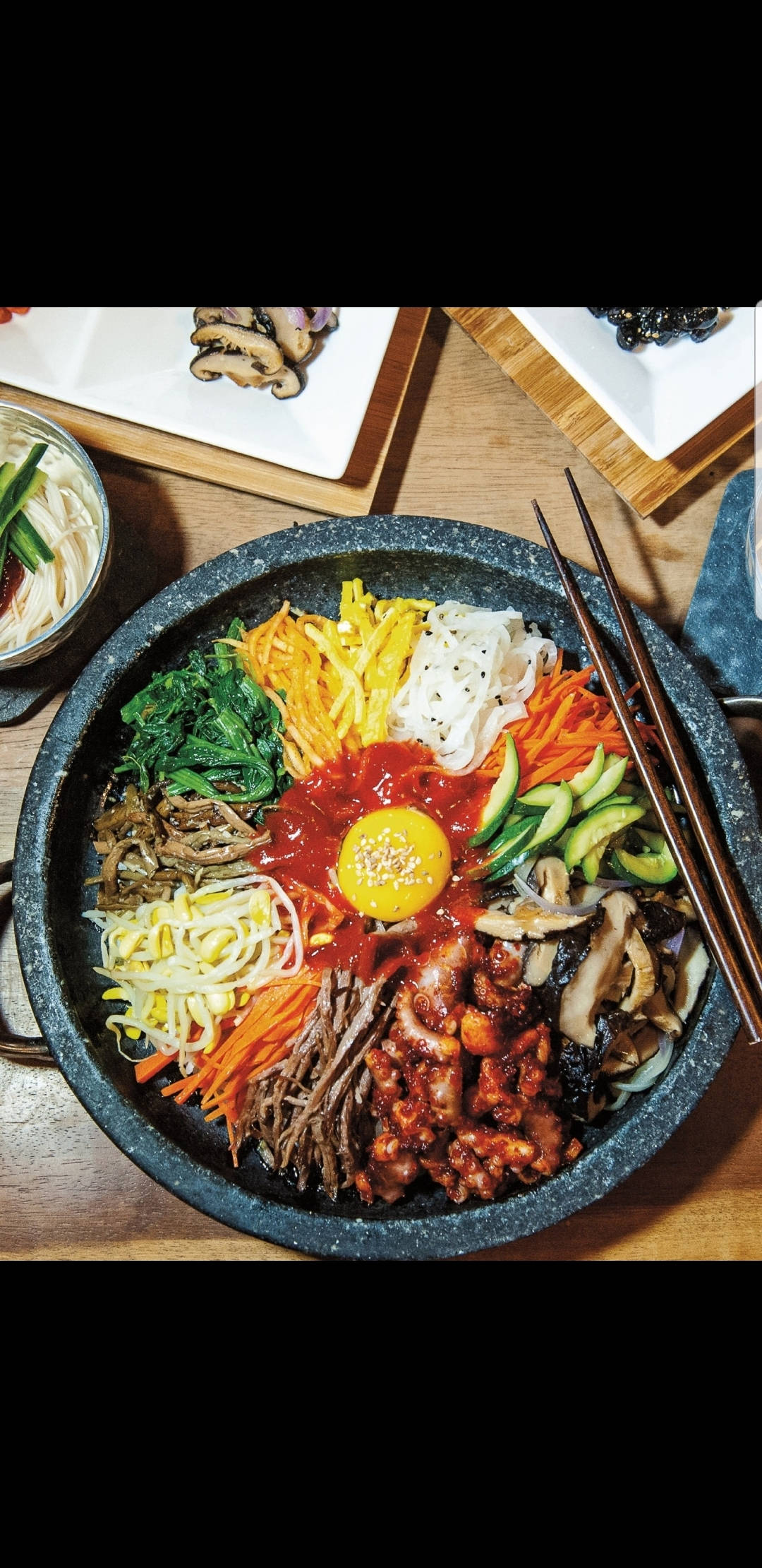 烹飪 桌布 壁紙 — 一個充滿活力的韓國石鍋拌飯，上面放著太陽蛋和色彩繽紛的蔬菜，放在木桌上。