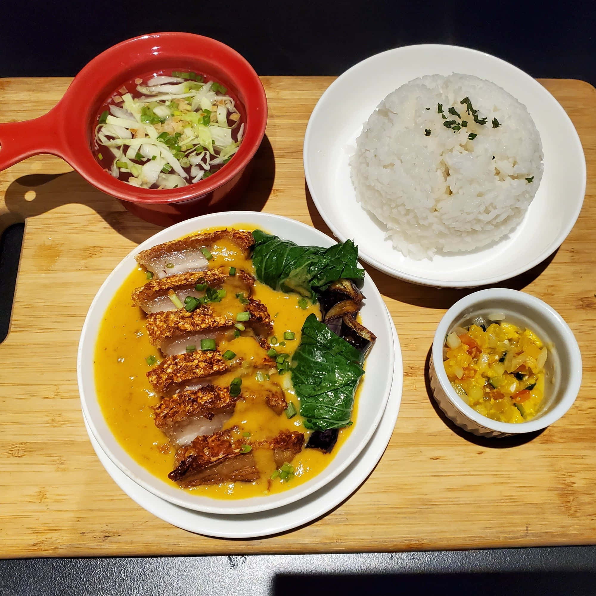 meat 桌布 壁紙 — 一個充滿活力的餐點，包括脆皮豬肉配黃色醬汁、米飯和配菜，放在木板上。