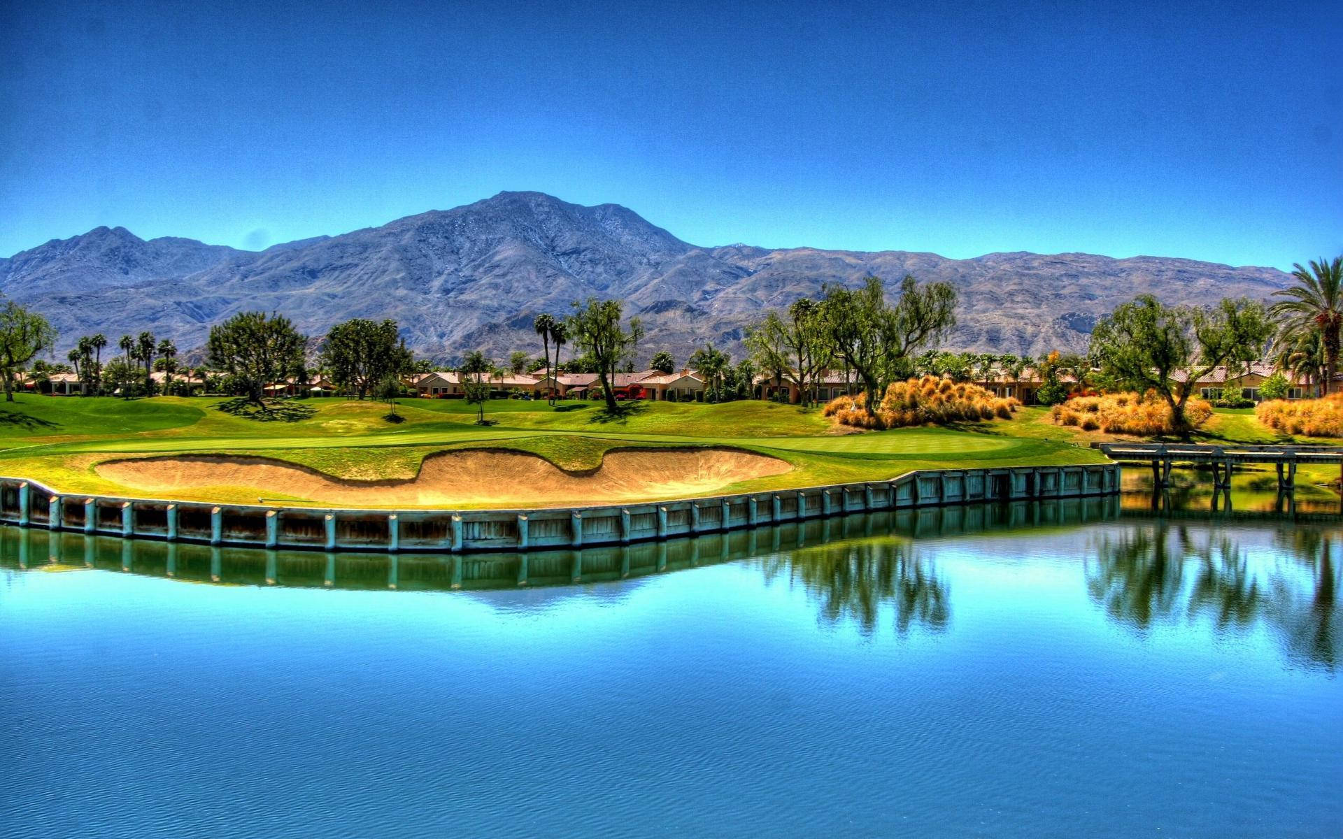 Golf Course Desktop 桌布 壁紙 — 一個充滿活力的高爾夫球場，設有水障礙和沙坑，在晴朗的藍天下映襯著遠山。