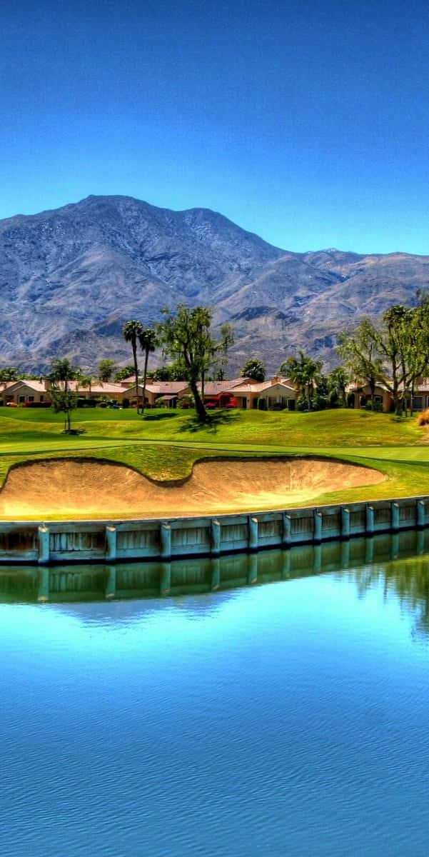 Pixel 3 Golf Course 桌布 壁紙 — 一個充滿活力的高爾夫球場，設有沙坑和寧靜的水塘，背景是晴朗藍天下的遠山。
