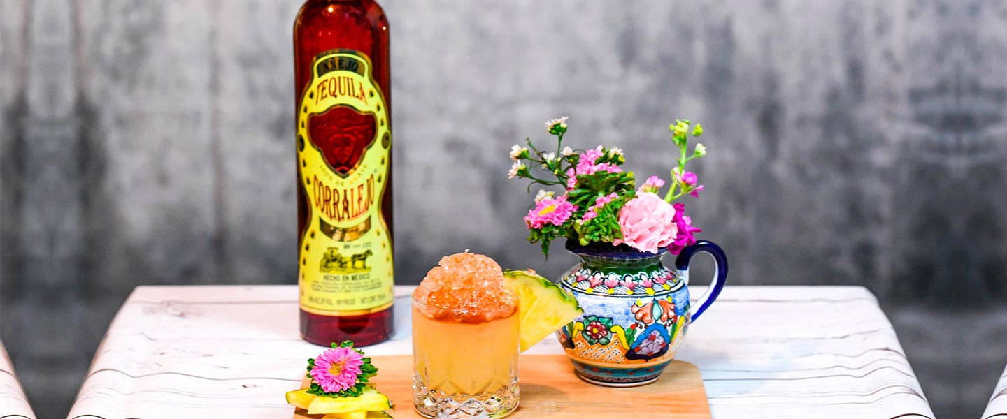 cocktail 桌布 壁紙 — 一個充滿活力的龍舌蘭酒瓶旁邊放著一杯冰涼的雞尾酒和一個色彩繽紛的花卉水壺，放在條紋桌布上。