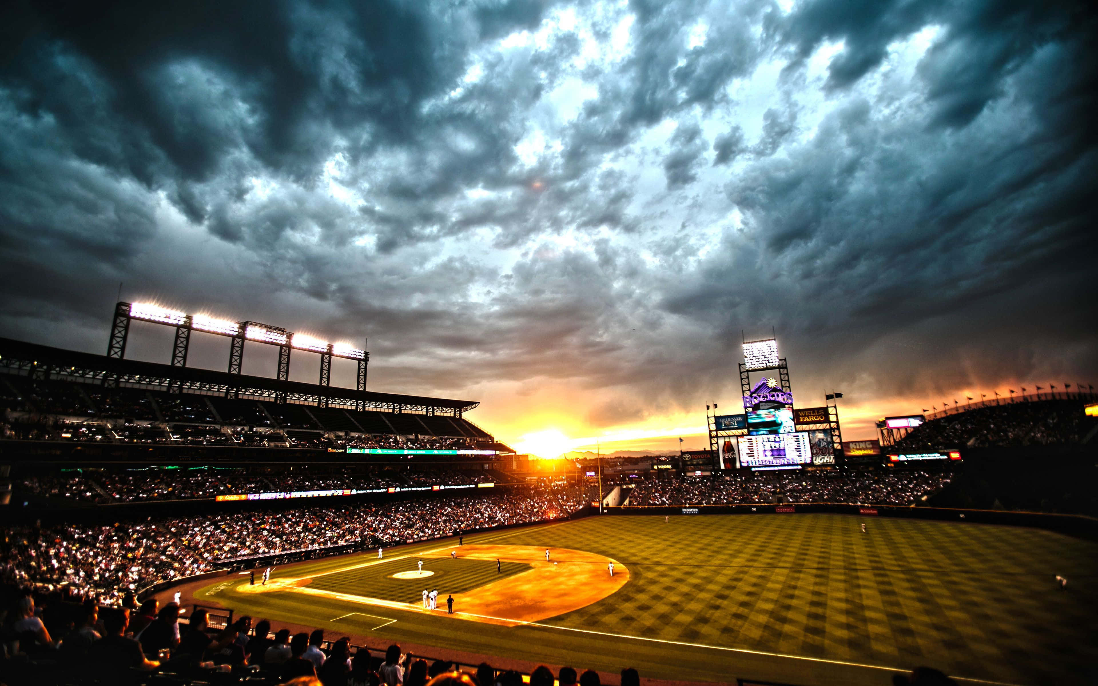 Baseball Stadium 桌布 壁紙 — 一個充滿球迷的棒球場，在帶有烏雲的戲劇性日落天空下。