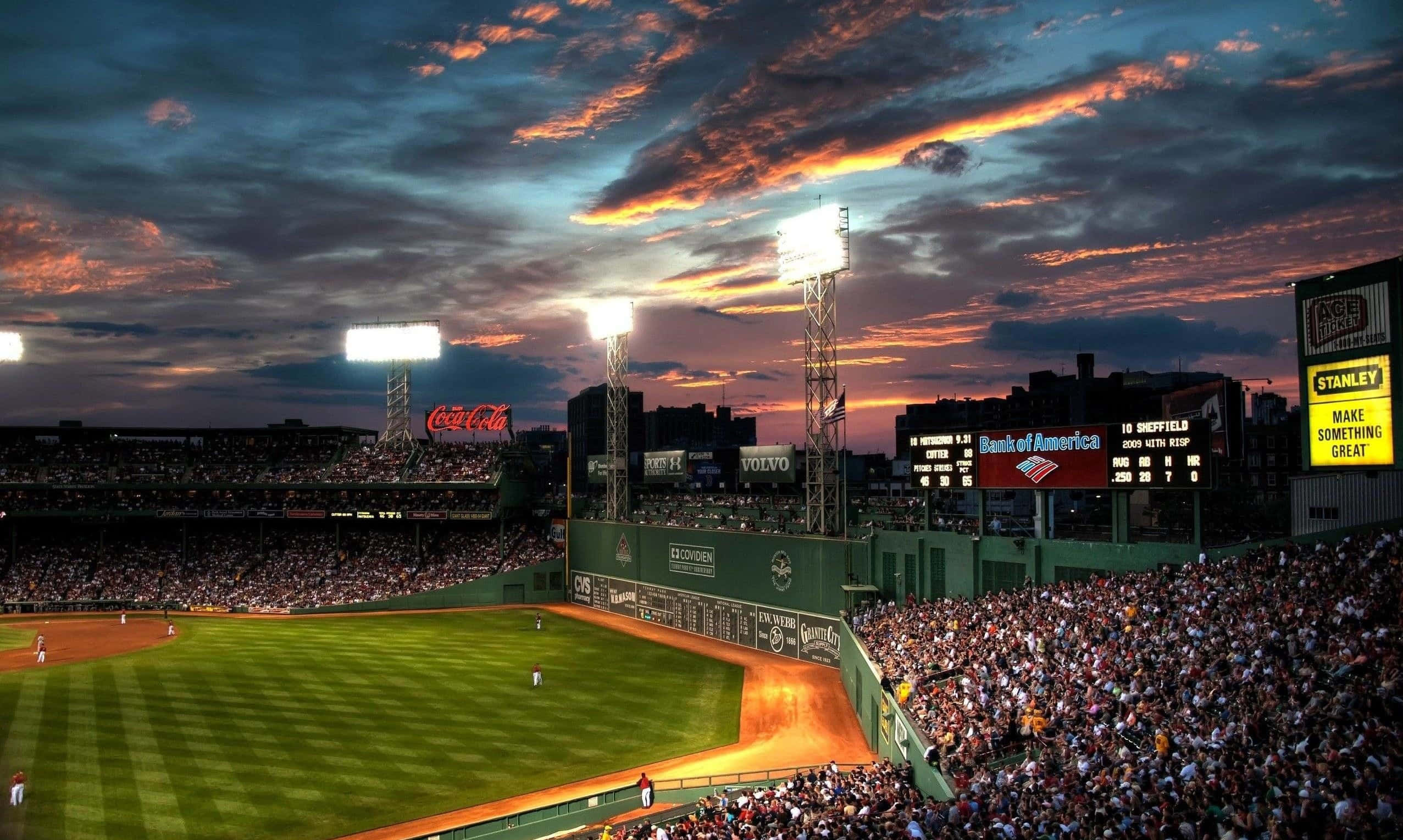 Baseball Stadium 桌布 壁紙 — 一個充滿球迷的棒球場，在橙紫色雲彩的戲劇性日落天空下。